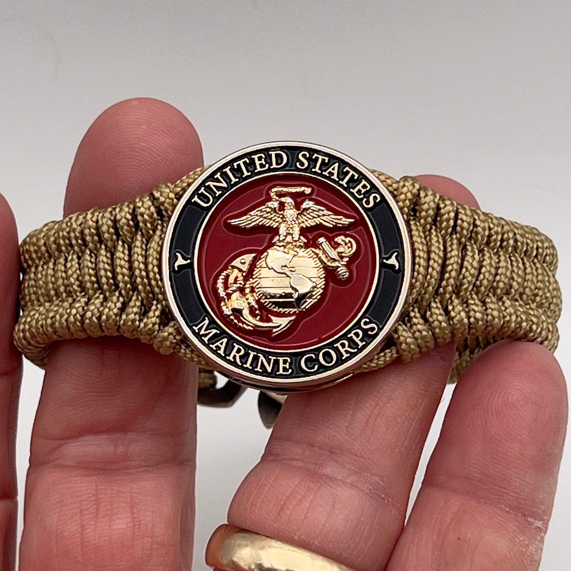 Thick, narrow, flexible and comfortable braided United States Marine Corps bracelet featuring a 24K gold plated USMC officer Eagle Globe and Anchor medallion, a gold Cobra style tactical buckle and woven with gold Type-1 paracord.