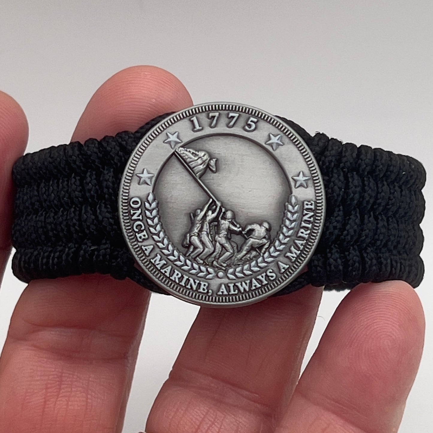 Thin, wide, flexible and comfortable braided United States Marine Corps Iwo Jima bracelet featuring an antique silver plated Iwo Jima flag raising medallion, a black Cobra style tactical buckle and woven with black Type-1 paracord.