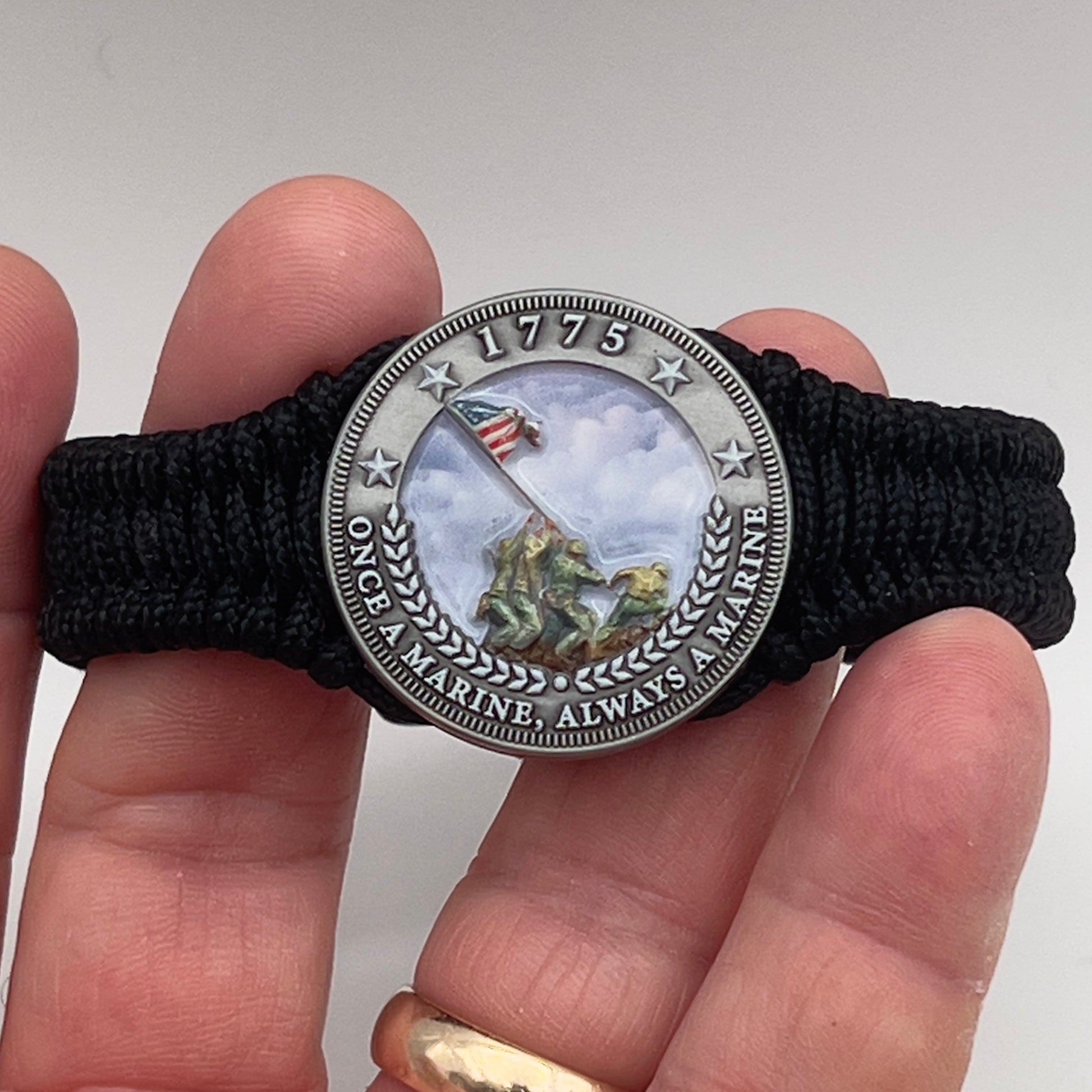 Thin, narrow and comfortable braided United States Marine Corps Iwo Jima bracelet featuring an antique silver plated UV painted Iwo Jima flag raising medallion, a black Cobra style tactical buckle and woven with black type-1 paracord.