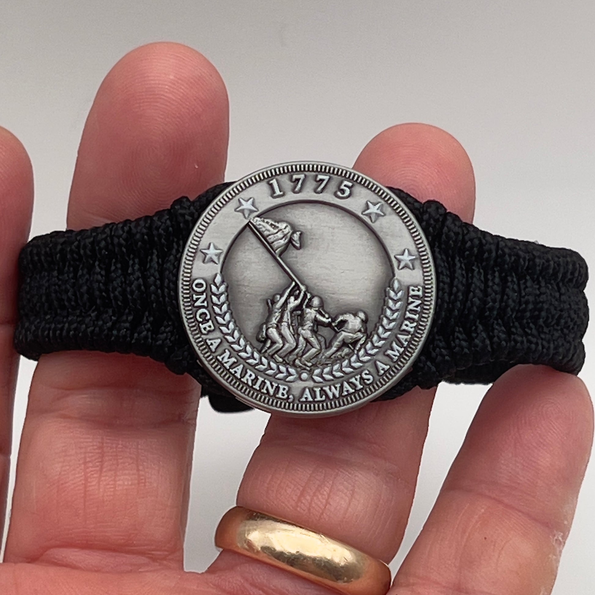 Thin, narrow and comfortable braided United States Marine Corps Iwo Jima bracelet featuring an antique silver plated Iwo Jima flag raising medallion, a black Cobra style tactical buckle and woven with black type-1 paracord.