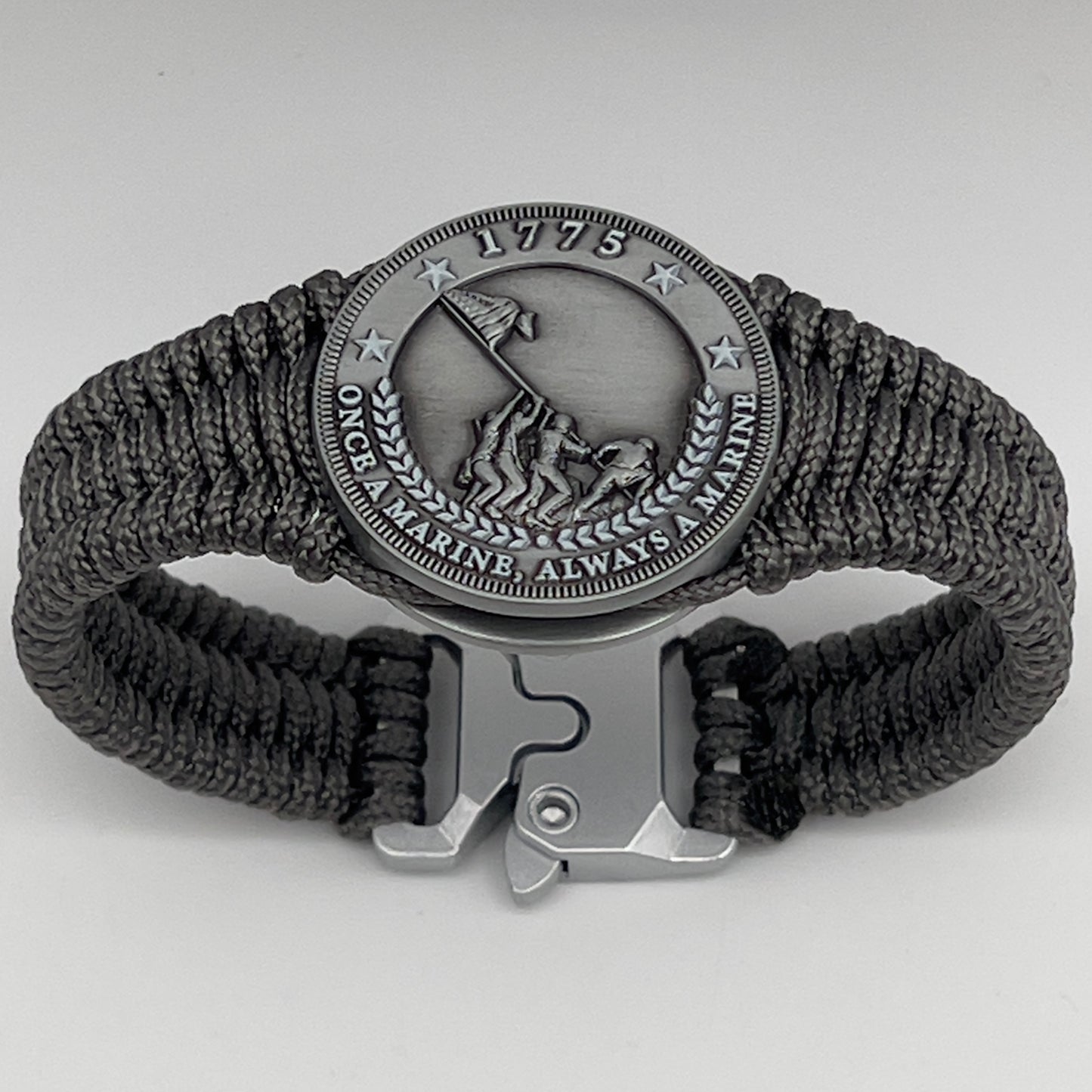 Thin, narrow, flexible and comfortable braided United States Marine Corps Iwo Jima bracelet featuring an antique silver plated Iwo Jima flag raising medallion, a silver Cobra style tactical buckle and woven with Charcoal Gray type-1 paracord.