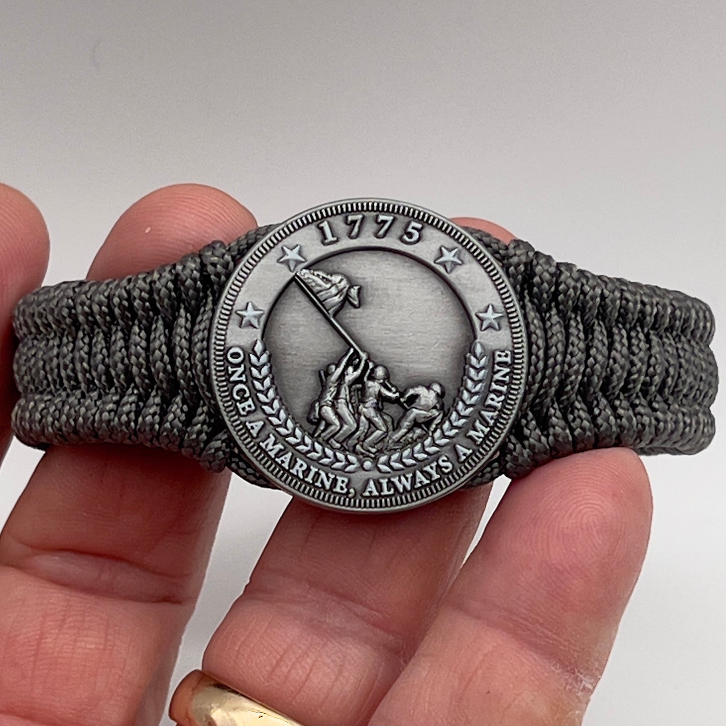 Thin, narrow, flexible and comfortable braided United States Marine Corps Iwo Jima bracelet featuring an antique silver plated Iwo Jima flag raising medallion, a silver Cobra style tactical buckle and woven with Charcoal Gray type-1 paracord.