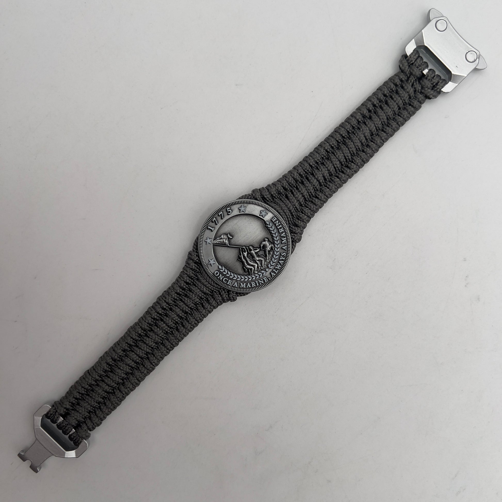 Thin, narrow, flexible and comfortable braided United States Marine Corps Iwo Jima bracelet featuring an antique silver plated Iwo Jima flag raising medallion, a silver Cobra style tactical buckle and woven with Charcoal Gray type-1 paracord.