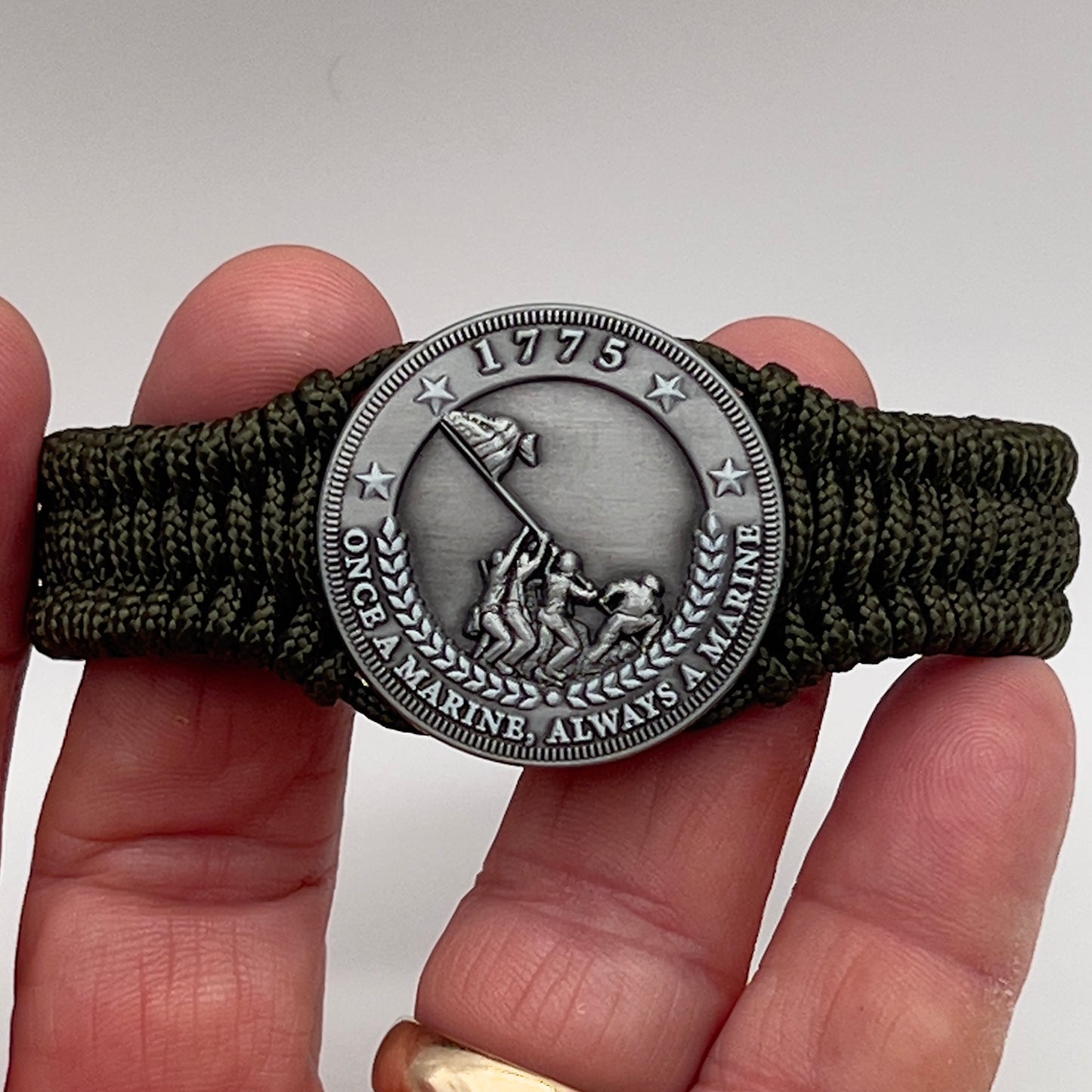 Thin, narrow, flexible and comfortable braided United States Marine Corps Iwo Jima bracelet featuring an antique silver plated UV painted Iwo Jima flag raising medallion, a silver Cobra style tactical buckle and woven with Olive Drab type-1 paracord.