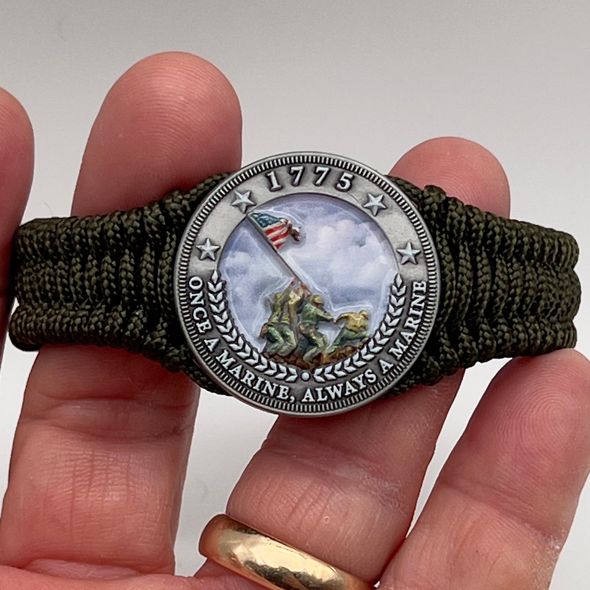 Thin, narrow, flexible and comfortable braided United States Marine Corps Iwo Jima bracelet featuring an antique silver plated UV painted Iwo Jima flag raising medallion, a silver Cobra style tactical buckle and woven with Olive Drab type-1 paracord.