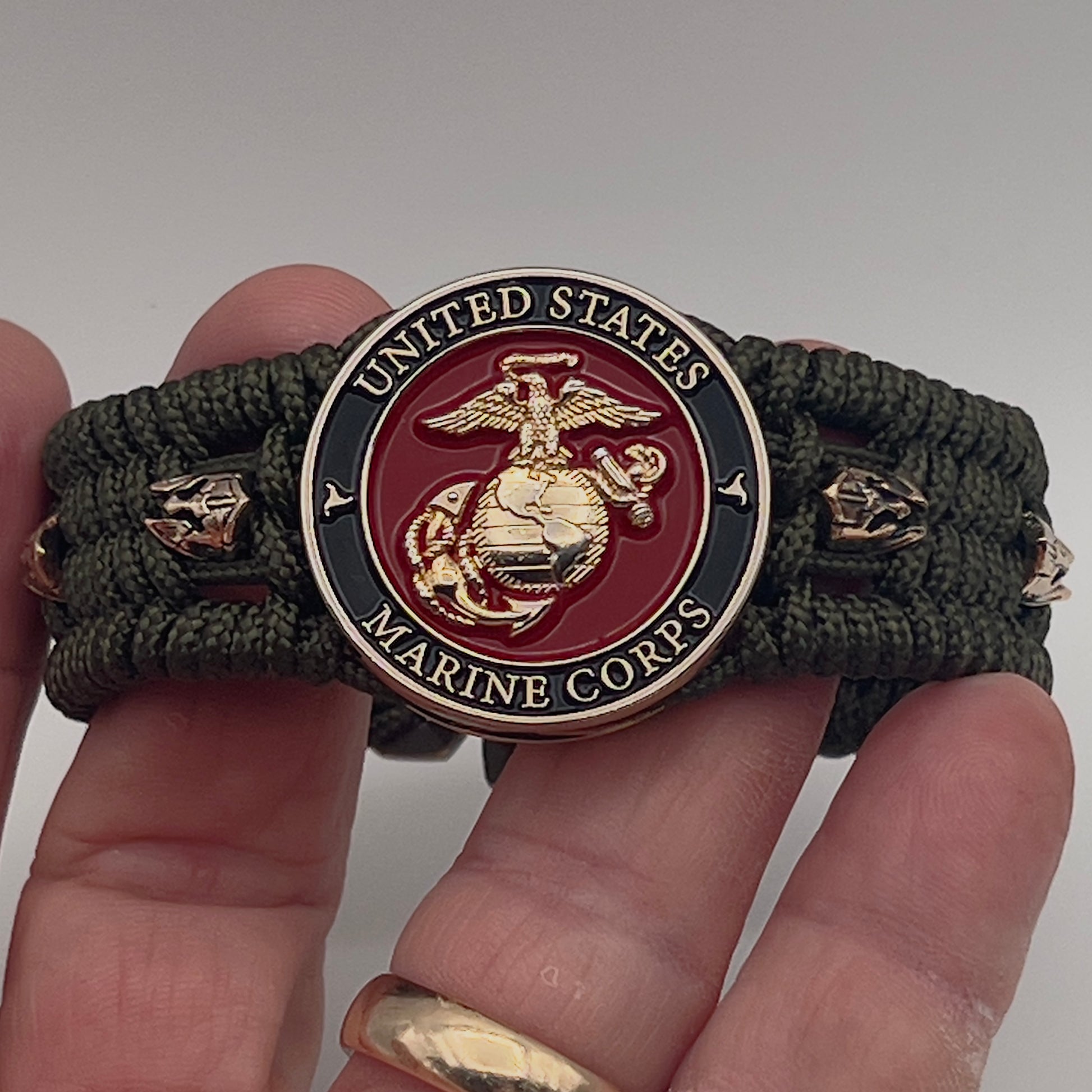 Thin, medium width, flexible and comfortable braided United States Marine Corps bracelet featuring a 24K gold plated USMC officer Eagle Globe and Anchor medallion, six Spartan micro beads, a gold Cobra style tactical buckle and woven with Olive Drab Type-1 paracord.