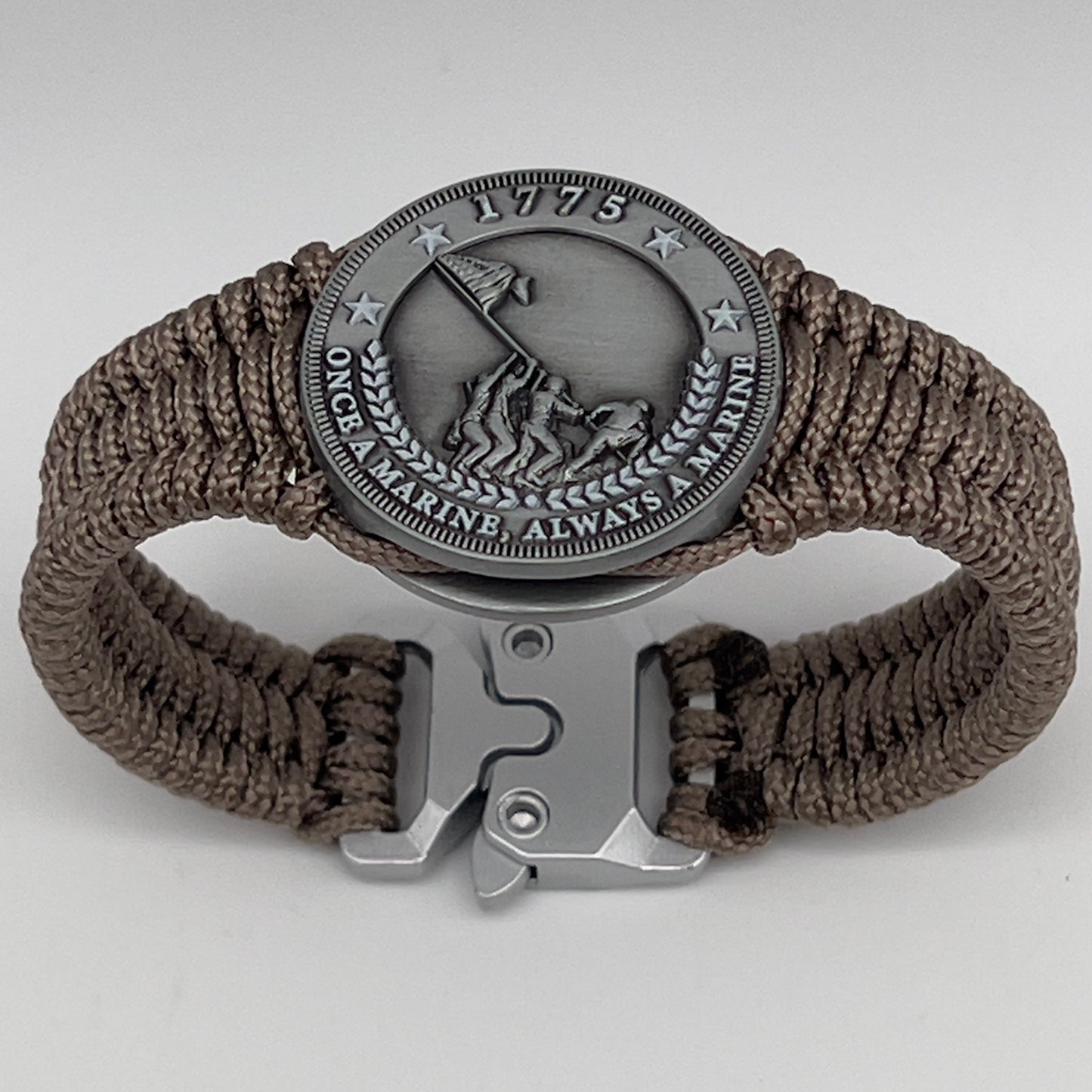 Thin, narrow, flexible and comfortable braided United States Marine Corps Iwo Jima bracelet featuring an antique silver plated Iwo Jima flag raising medallion, a silver Cobra style tactical buckle and woven with tan type-1 paracord.