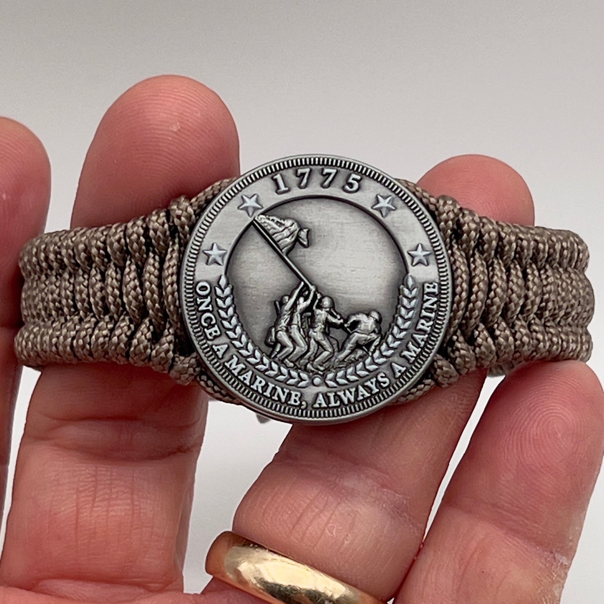 Thin, narrow, flexible and comfortable braided United States Marine Corps Iwo Jima bracelet featuring an antique silver plated Iwo Jima flag raising medallion, a silver Cobra style tactical buckle and woven with tan type-1 paracord.