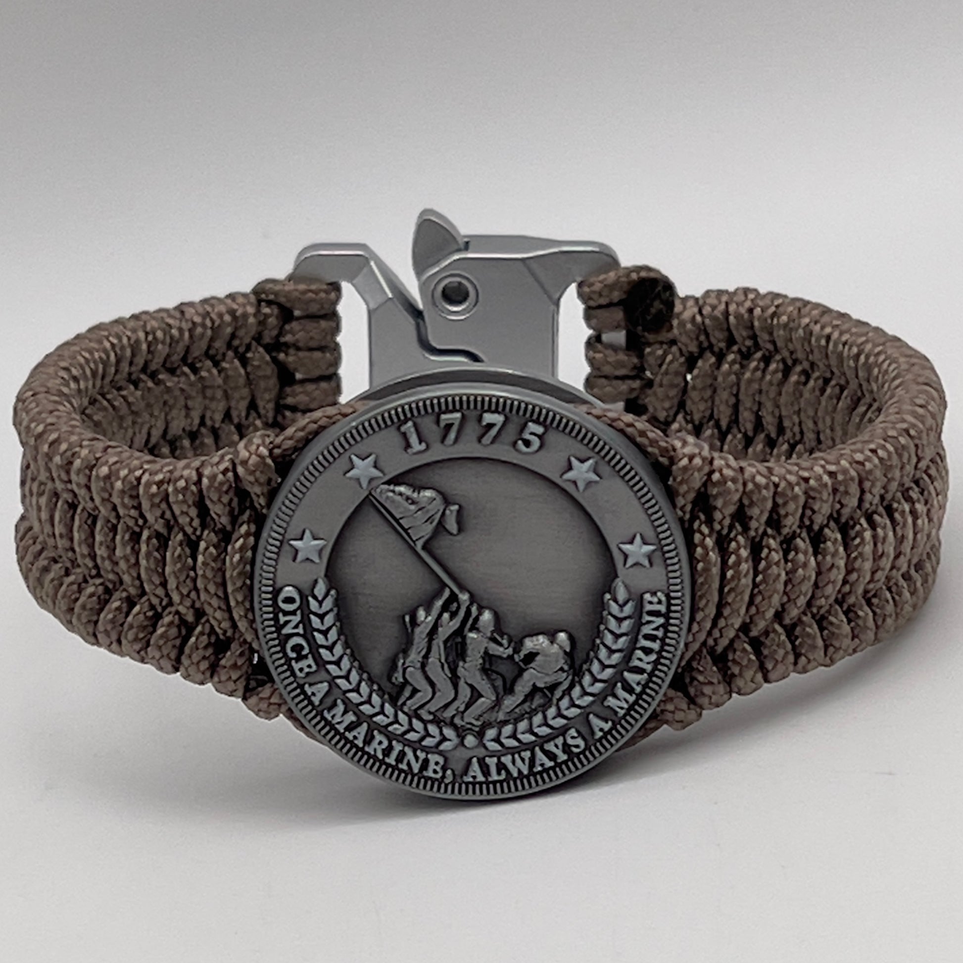 Thin, narrow, flexible and comfortable braided United States Marine Corps Iwo Jima bracelet featuring an antique silver plated Iwo Jima flag raising medallion, a silver Cobra style tactical buckle and woven with tan type-1 paracord.