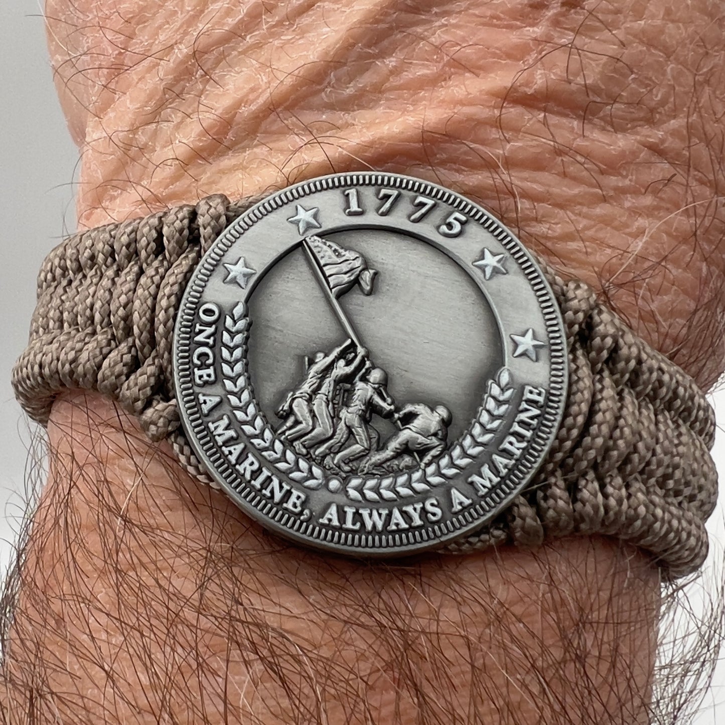Thin, narrow, flexible and comfortable braided United States Marine Corps Iwo Jima bracelet featuring an antique silver plated Iwo Jima flag raising medallion, a silver Cobra style tactical buckle and woven with tan type-1 paracord.
