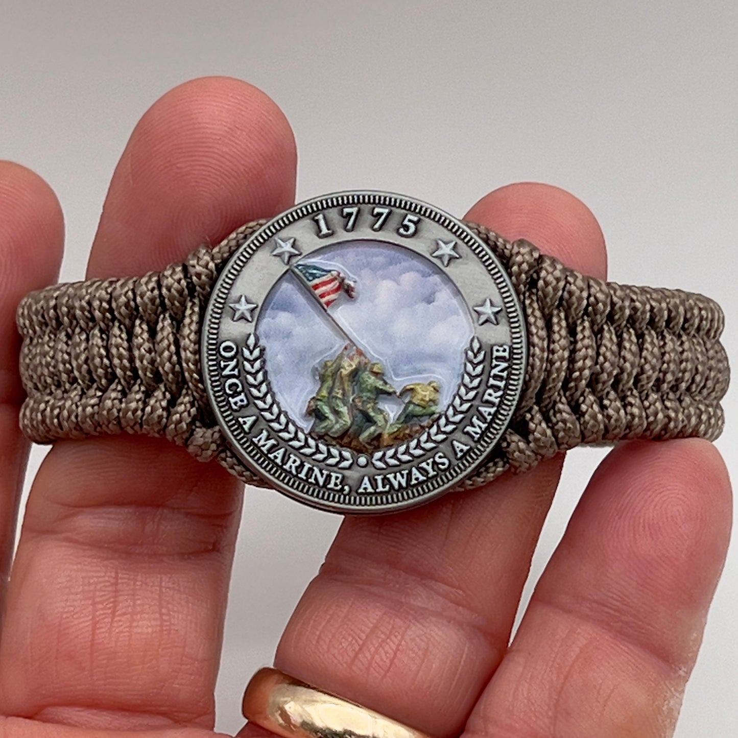 Thin, narrow, flexible and comfortable braided United States Marine Corps Iwo Jima bracelet featuring an antique silver plated UV painted Iwo Jima flag raising medallion, a silver Cobra style tactical buckle and woven with tan type-1 paracord.