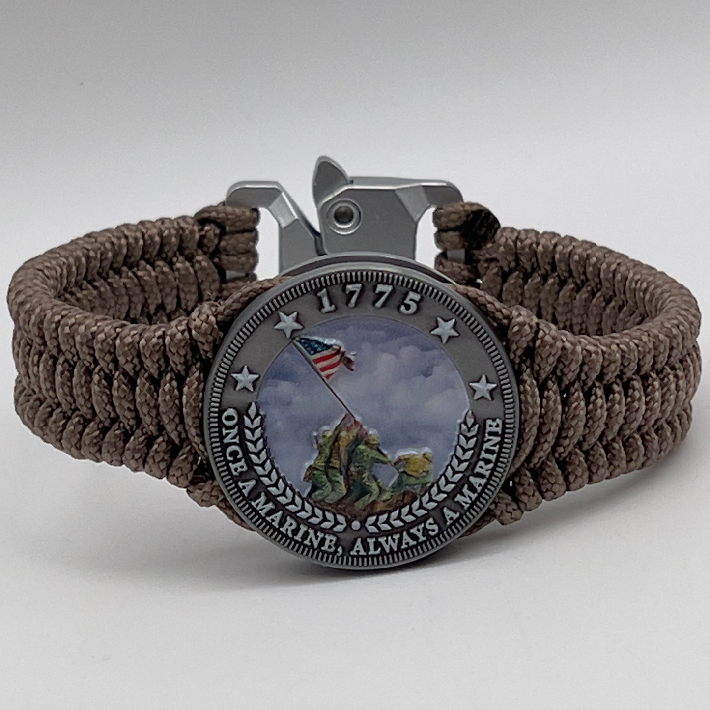 Thin, narrow, flexible and comfortable braided United States Marine Corps Iwo Jima bracelet featuring an antique silver plated UV painted Iwo Jima flag raising medallion, a silver Cobra style tactical buckle and woven with tan type-1 paracord.