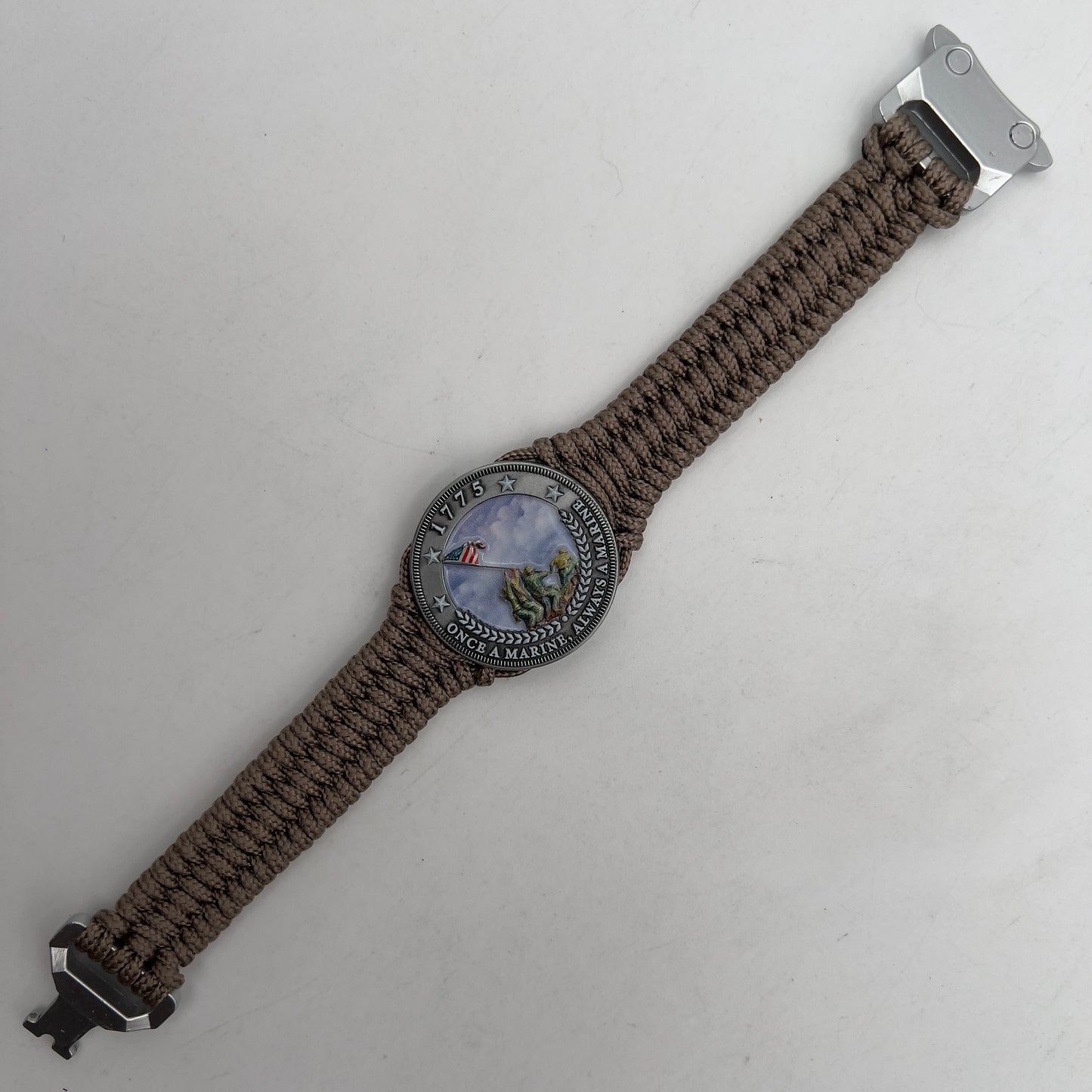 Thin, narrow, flexible and comfortable braided United States Marine Corps Iwo Jima bracelet featuring an antique silver plated UV painted Iwo Jima flag raising medallion, a silver Cobra style tactical buckle and woven with tan type-1 paracord.