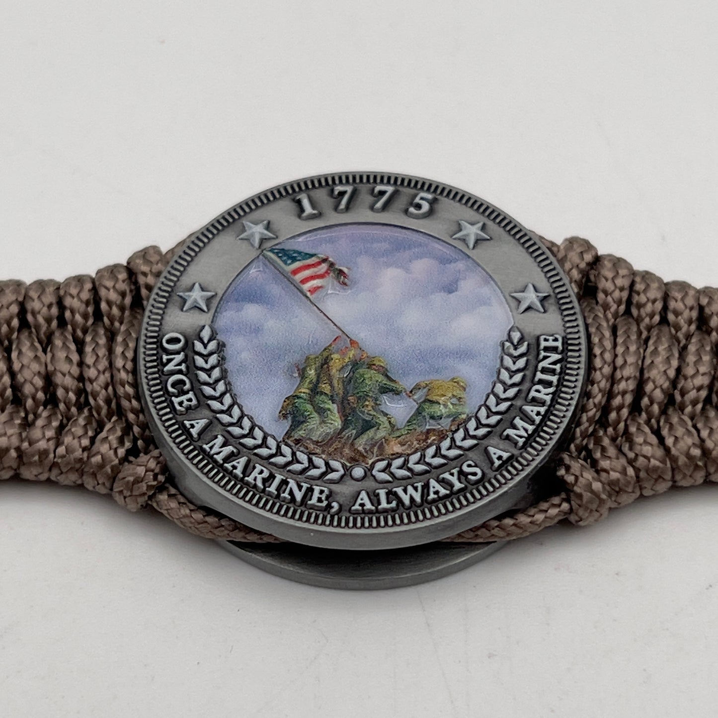 Thin, narrow, flexible and comfortable braided United States Marine Corps Iwo Jima bracelet featuring an antique silver plated UV painted Iwo Jima flag raising medallion, a silver Cobra style tactical buckle and woven with tan type-1 paracord.