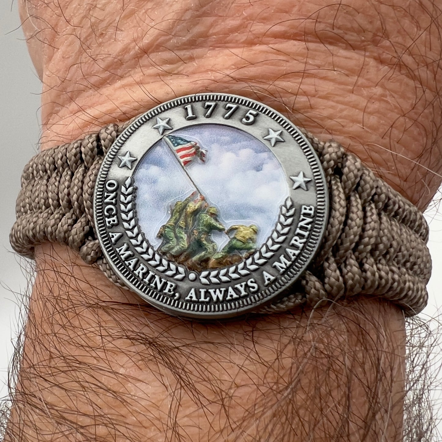 Thin, narrow, flexible and comfortable braided United States Marine Corps Iwo Jima bracelet featuring an antique silver plated UV painted Iwo Jima flag raising medallion, a silver Cobra style tactical buckle and woven with tan type-1 paracord.