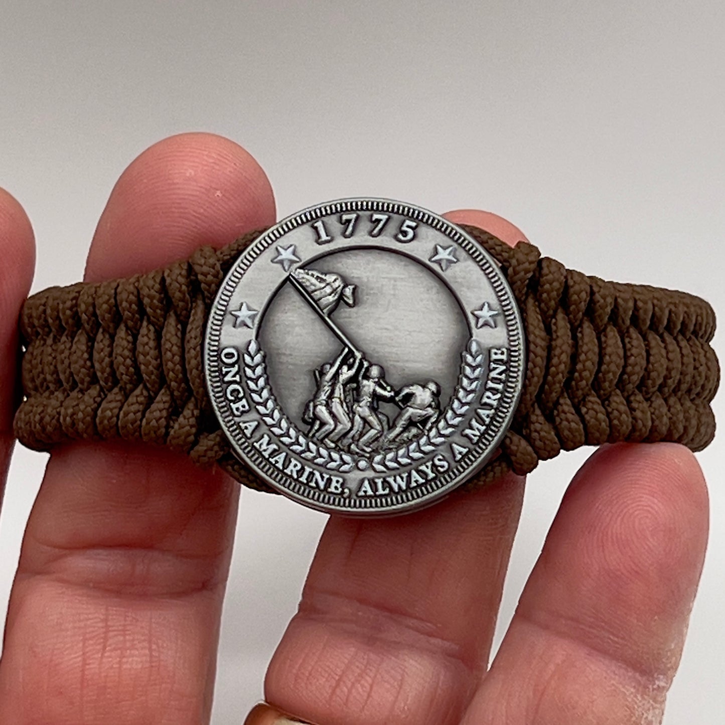 Thin, narrow, flexible and comfortable braided United States Marine Corps Iwo Jima bracelet featuring an antique silver plated Iwo Jima flag raising medallion, a silver Cobra style tactical buckle and woven with Coyote Brown type-1 paracord.
