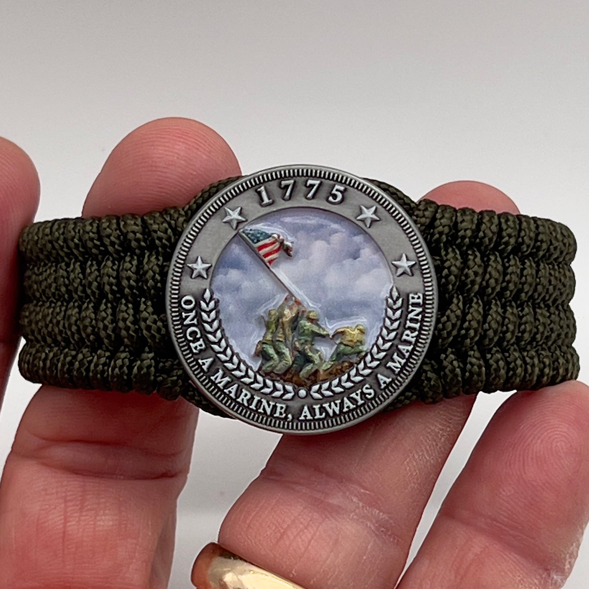 Thin, wide, flexible and comfortable braided United States Marine Corps Iwo Jima bracelet featuring an antique silver plated UV painted Iwo Jima flag raising medallion, a silver Cobra style tactical buckle and woven with olive drab Type-1 paracord.