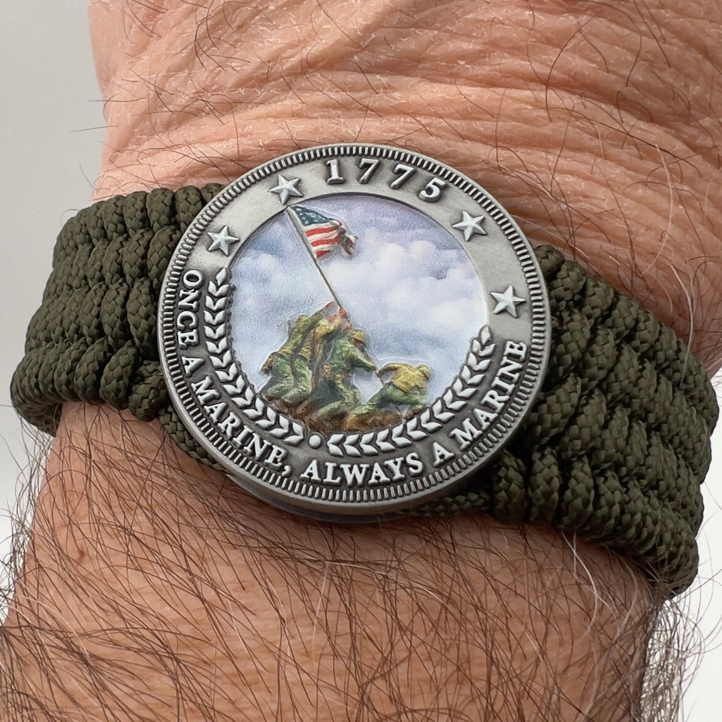 Thin, wide, flexible and comfortable braided United States Marine Corps Iwo Jima bracelet featuring an antique silver plated UV painted Iwo Jima flag raising medallion, a silver Cobra style tactical buckle and woven with olive drab Type-1 paracord.