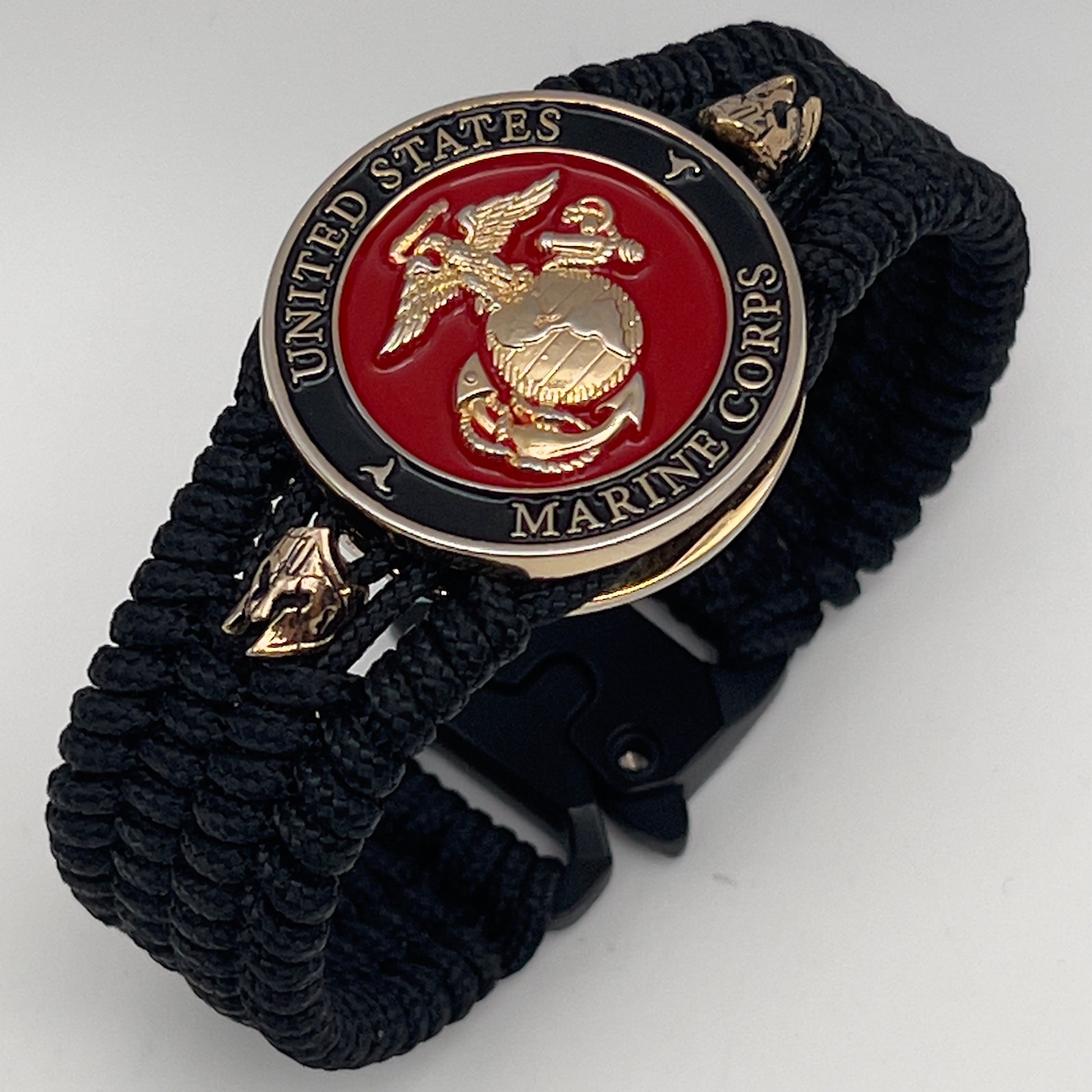 Thin, medium width, flexible and comfortable braided United States Marine Corps bracelet featuring a 24K gold plated USMC officer Eagle Globe and Anchor medallion, two brass Spartan helmets, a black Cobra style tactical buckle and woven with black Type-1 paracord.