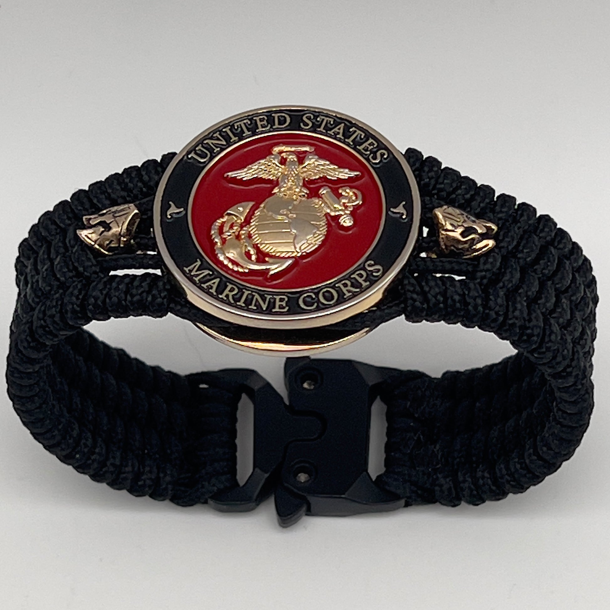 Thin, medium width, flexible and comfortable braided United States Marine Corps bracelet featuring a 24K gold plated USMC officer Eagle Globe and Anchor medallion, two brass Spartan helmets, a black Cobra style tactical buckle and woven with black Type-1 paracord.