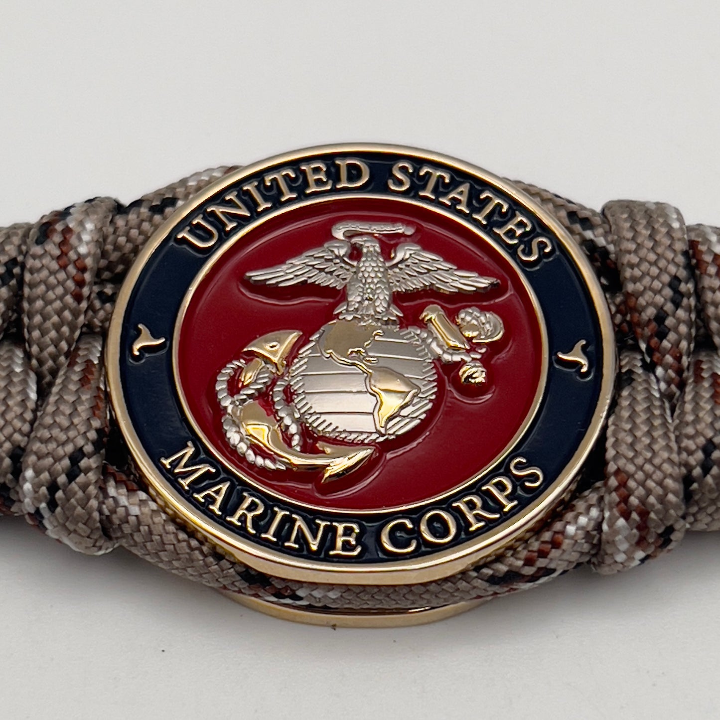 Thick and comfortable braided United States Marine Corps bracelet featuring a 24K gold and silver plated USMC officer Eagle Globe and Anchor medallion, a Cobra style tactical buckle and woven with Desert Camo paracord.