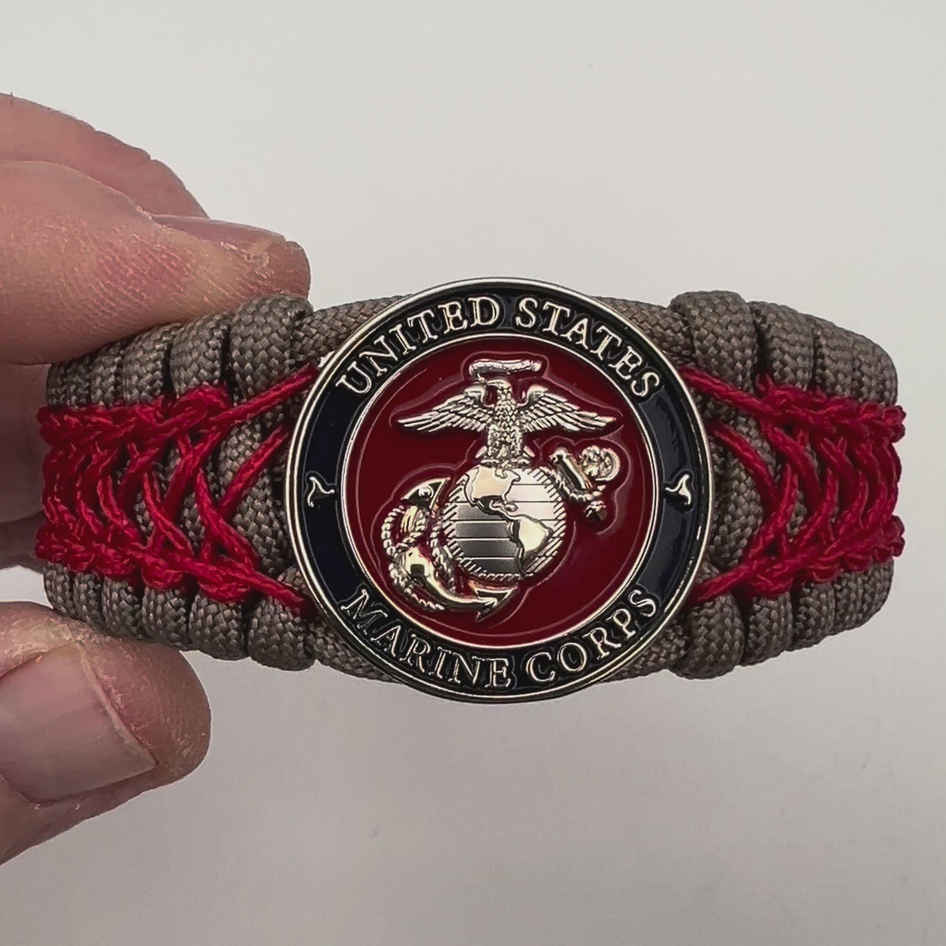 Thick, semi-rigid and comfortable braided United States Marine Corps bracelet featuring a 24K gold and silver plated USMC officer Eagle Globe and Anchor medallion, a gold Cobra style tactical buckle and woven with tan 550 paracord and Imperial red micro cord.
