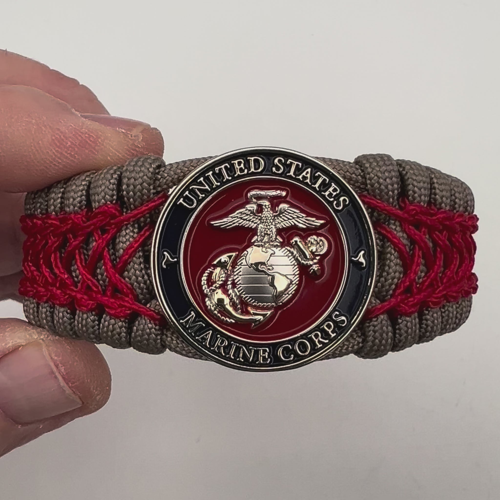 Thick, semi-rigid and comfortable braided United States Marine Corps bracelet featuring a 24K gold and silver plated USMC officer Eagle Globe and Anchor medallion, a gold Cobra style tactical buckle and woven with tan 550 paracord and Imperial red micro cord.