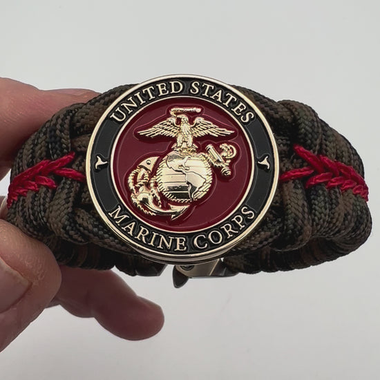 Thick, rigid and comfortable braided United States Marine Corps bracelet featuring a 24K gold plated USMC Eagle Globe and Anchor medallion, a gold Cobra style tactical buckle and woven with Woodland Camo 550 paracord and Imperial Red micro cord.