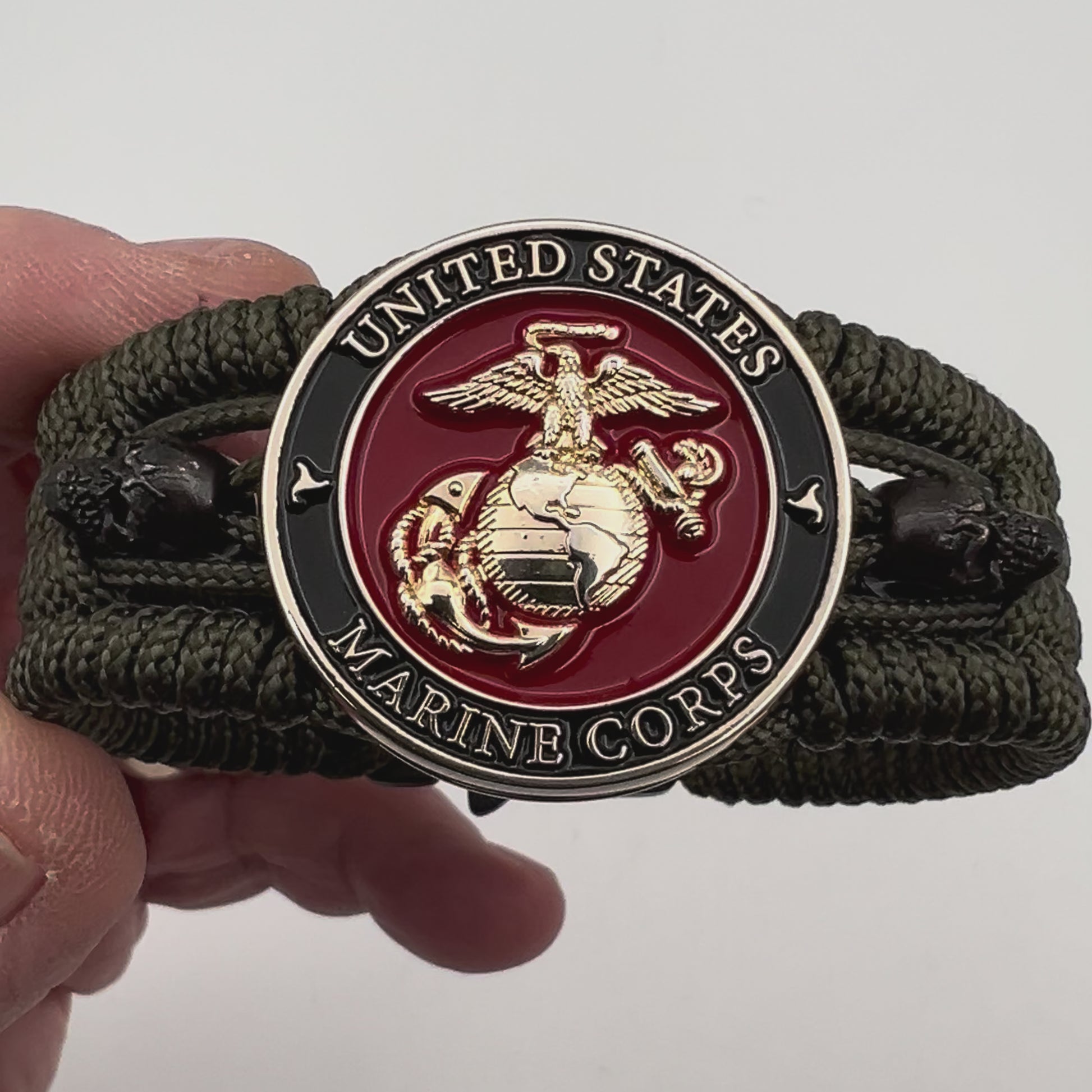 Thin, medium width, flexible and comfortable braided United States Marine Corps bracelet featuring a 24K gold plated USMC officer Eagle Globe and Anchor medallion, two black micro skulls, a black Cobra style tactical buckle and woven with Olive Drab Type-1 paracord.