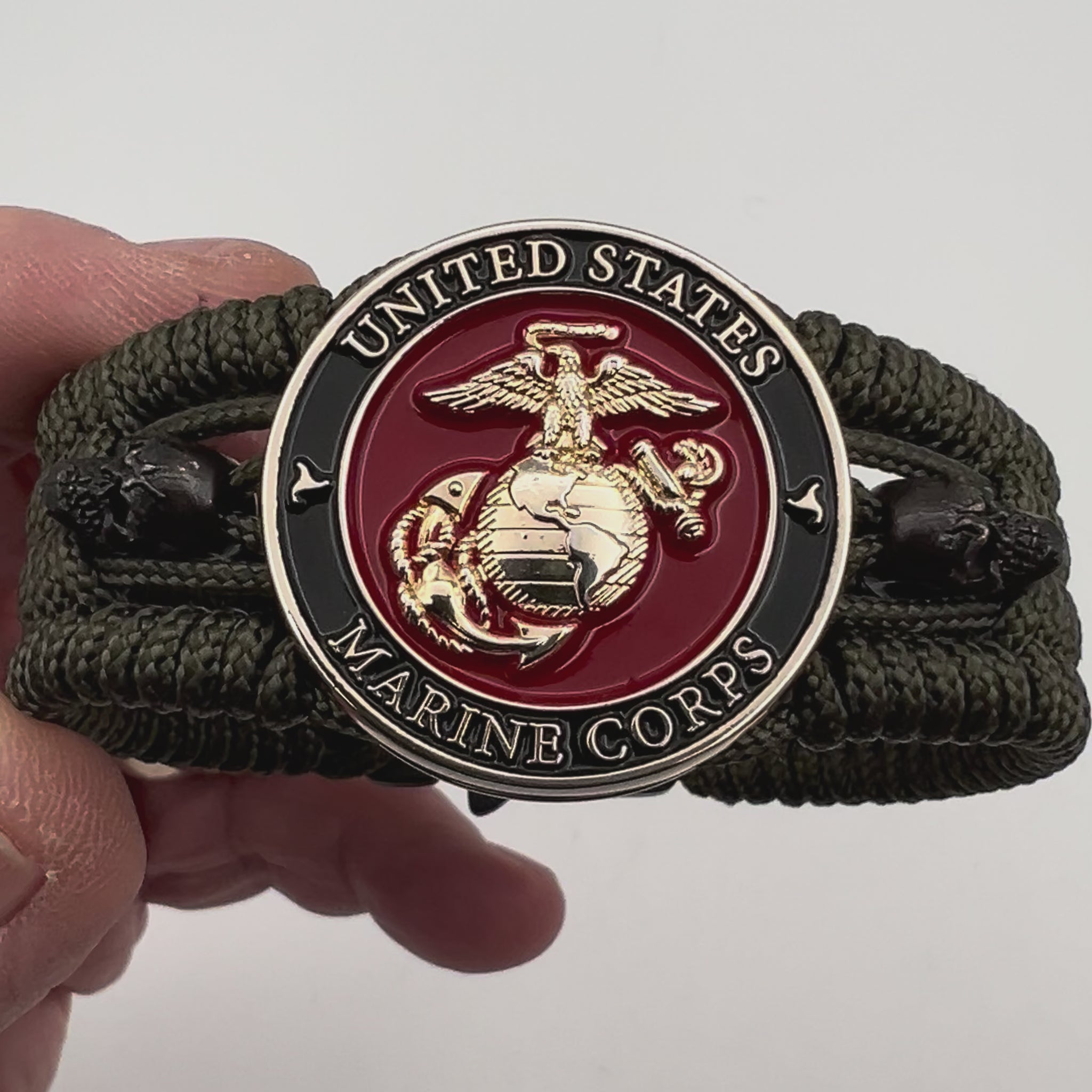 Thin, medium width, flexible and comfortable braided United States Marine Corps bracelet featuring a 24K gold plated USMC officer Eagle Globe and Anchor medallion, two black micro skulls, a black Cobra style tactical buckle and woven with Olive Drab Type-1 paracord.