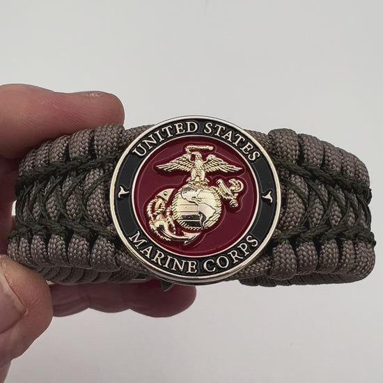 Thick, wide, rigid and comfortable braided United States Marine Corps bracelet featuring a 24K gold plated USMC Eagle Globe and Anchor medallion, a gold Cobra style tactical buckle and woven with tan 550 paracord and olive drab nano and micro cord.