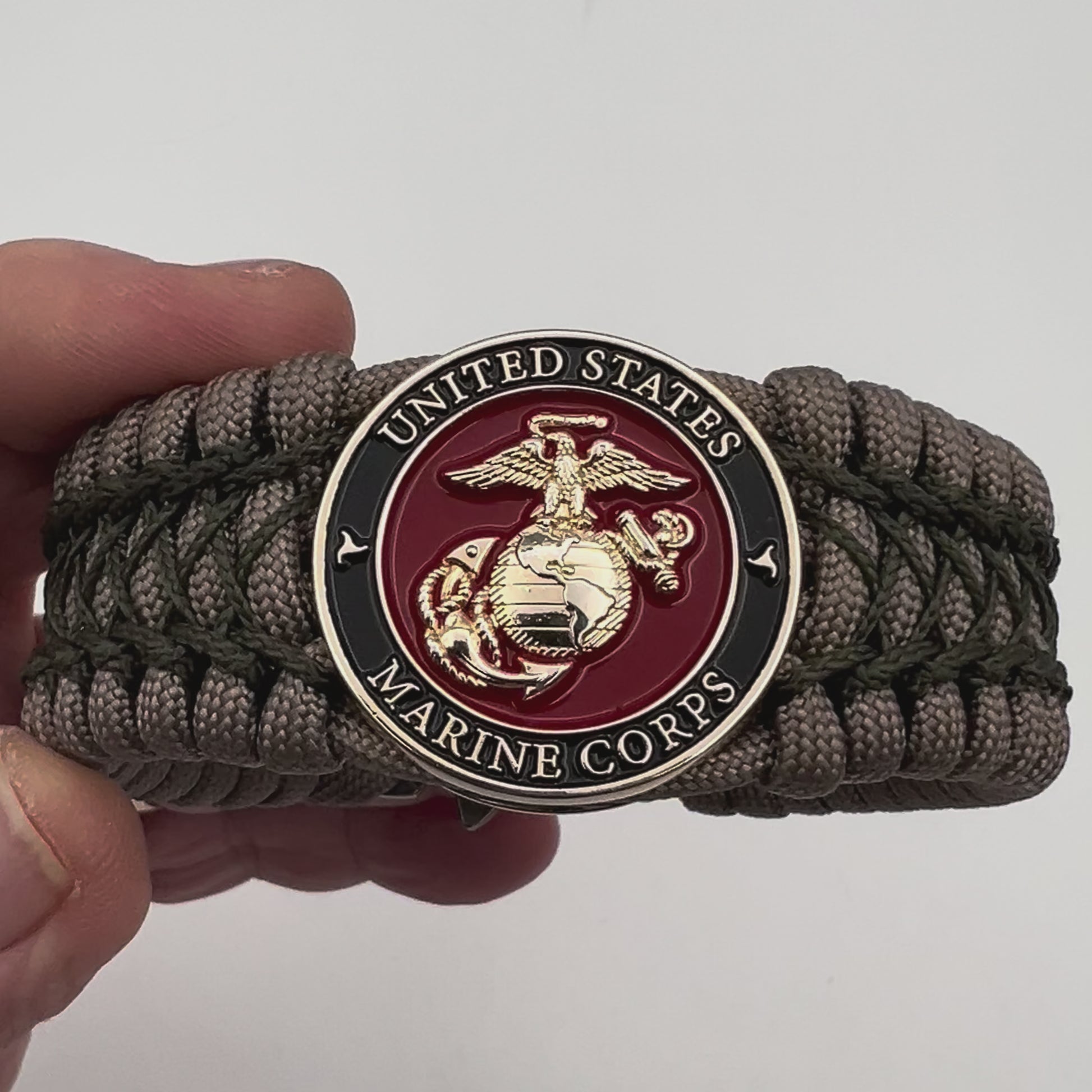 Thick, wide, rigid and comfortable braided United States Marine Corps bracelet featuring a 24K gold plated USMC Eagle Globe and Anchor medallion, a gold Cobra style tactical buckle and woven with tan 550 paracord and olive drab nano and micro cord.