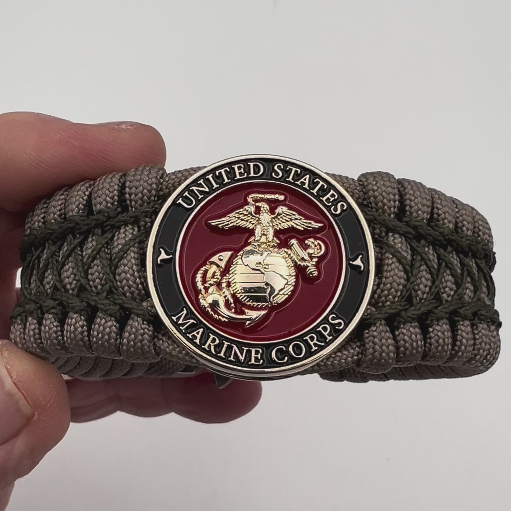 Thick, wide, rigid and comfortable braided United States Marine Corps bracelet featuring a 24K gold plated USMC Eagle Globe and Anchor medallion, a gold Cobra style tactical buckle and woven with tan 550 paracord and olive drab nano and micro cord.