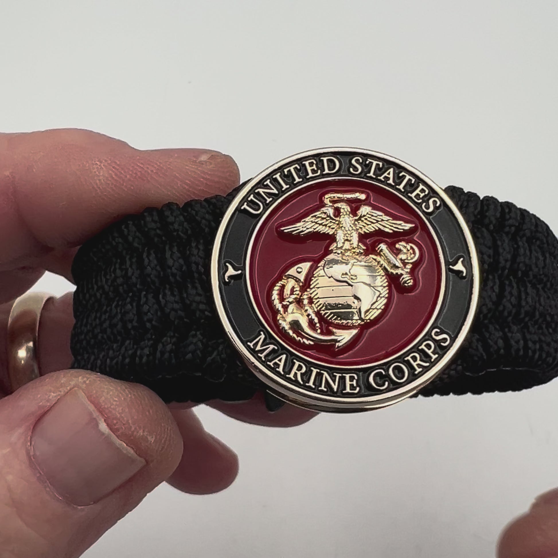 Thin, medium width, flexible and comfortable braided United States Marine Corps bracelet featuring a 24K gold plated USMC officer Eagle Globe and Anchor medallion, a black Cobra style tactical buckle and woven with black Type-1 paracord.