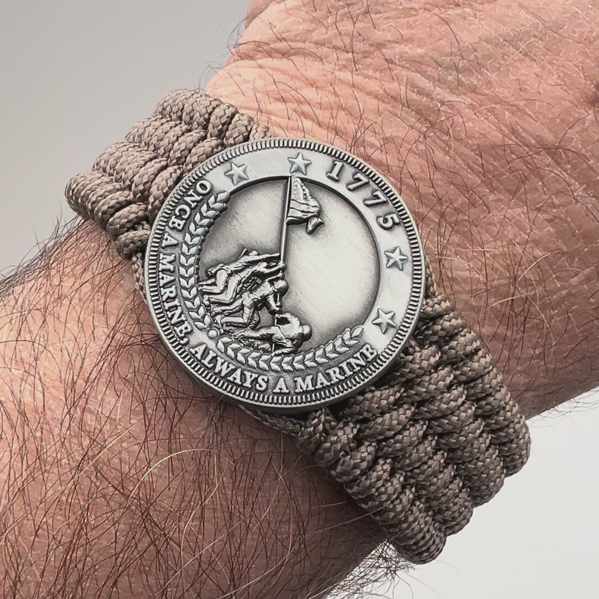 Thin, wide, flexible and comfortable braided United States Marine Corps Iwo Jima bracelet featuring an antique silver plated Iwo Jima flag raising medallion, a silver Cobra style tactical buckle and woven with tan type-1 paracord.