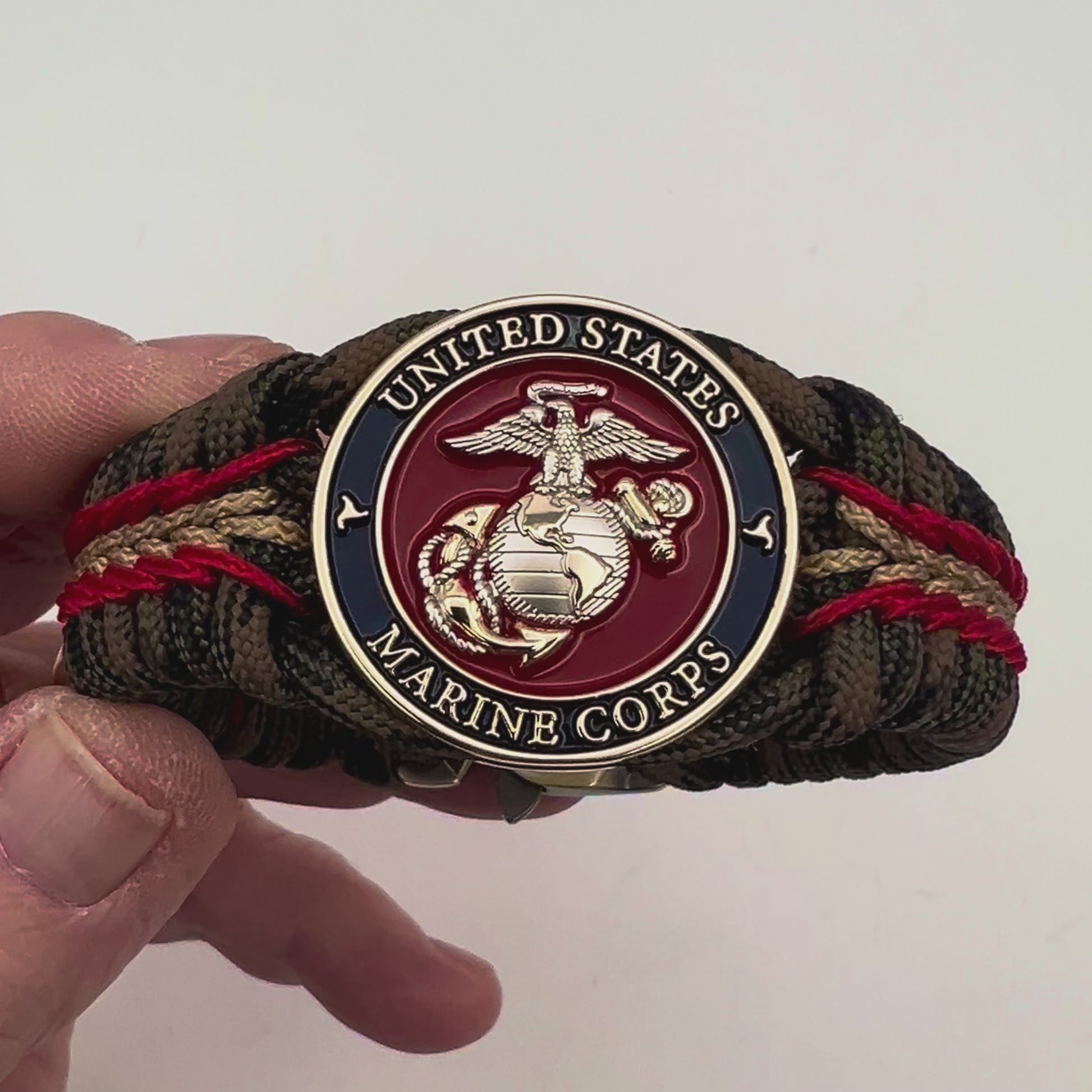 Thick, semi-rigid and comfortable braided United States Marine Corps bracelet featuring a 24K gold and silver plated USMC officer Eagle Globe and Anchor medallion, a gold Cobra style tactical buckle and woven with Woodland Camo 550 paracord and Imperial Red and gold micro cord.
