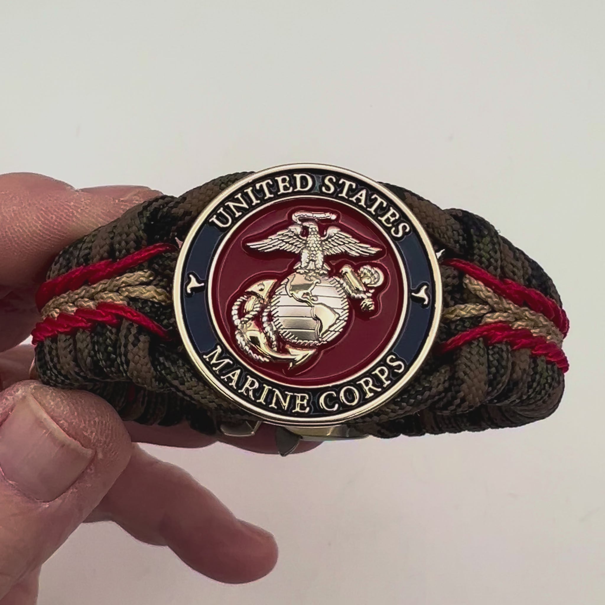 Thick, semi-rigid and comfortable braided United States Marine Corps bracelet featuring a 24K gold and silver plated USMC officer Eagle Globe and Anchor medallion, a gold Cobra style tactical buckle and woven with Woodland Camo 550 paracord and Imperial Red and gold micro cord.