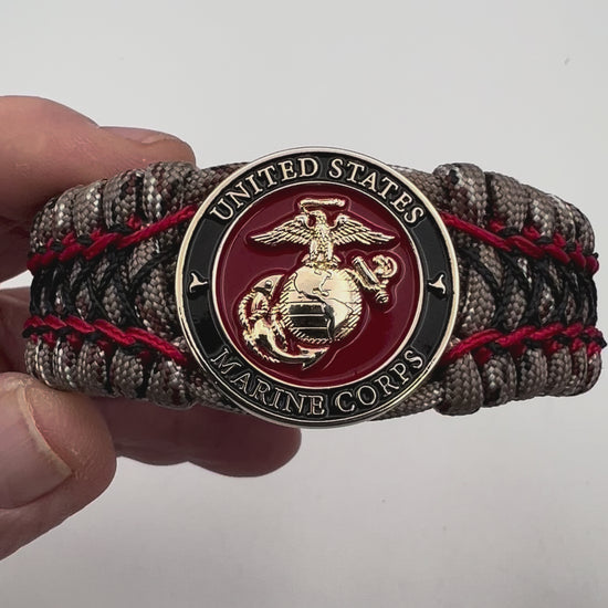 Thick, wide, rigid and comfortable braided United States Marine Corps bracelet featuring a 24K gold plated USMC Eagle Globe and Anchor medallion, a gold Cobra style tactical buckle and woven with Desert Camo 550 paracord, Imperial Red micro cord and black nano cord.