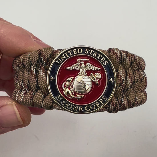 Thick and comfortable braided United States Marine Corps bracelet featuring a 24K gold and silver plated USMC officer Eagle Globe and Anchor medallion, a gold Cobra style tactical buckle and woven with Desert Camo 550 paracord.
