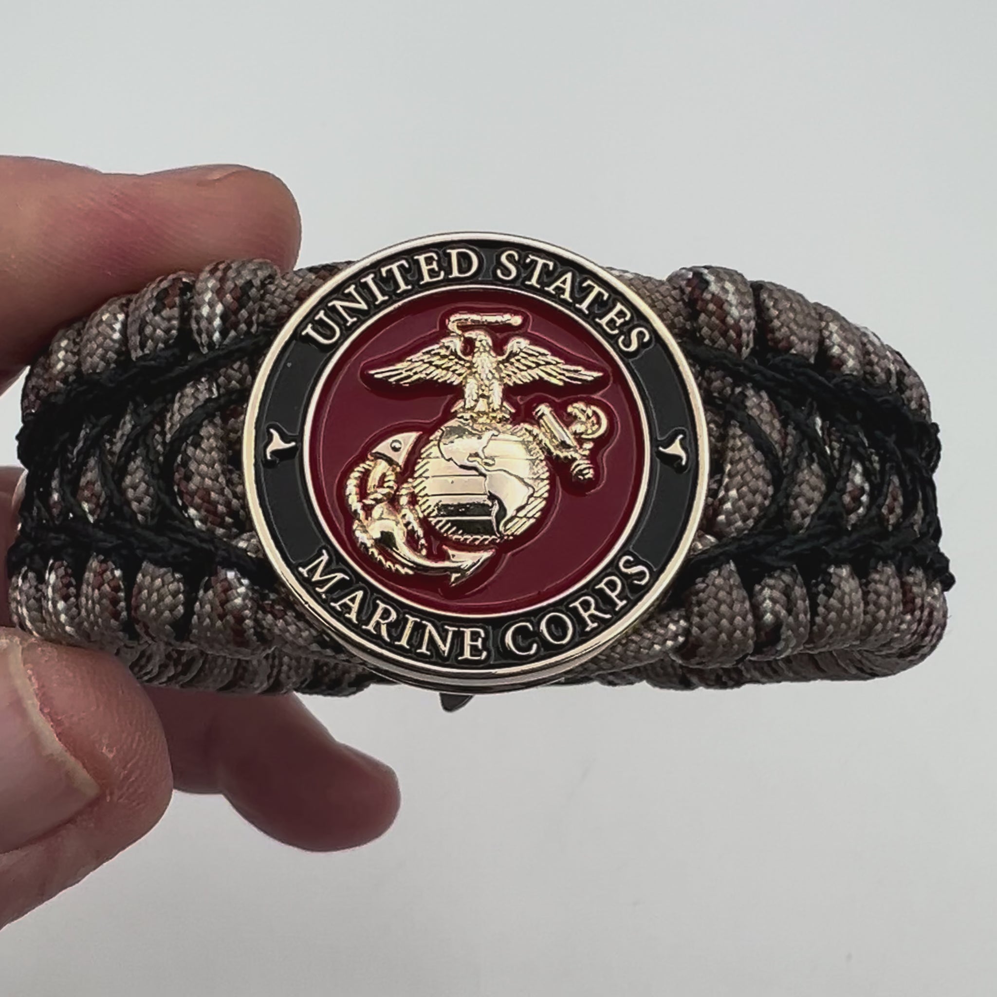Thick, wide, rigid and comfortable braided United States Marine Corps bracelet featuring a 24K gold plated USMC Eagle Globe and Anchor medallion, a gold Cobra style tactical buckle and woven with Desert Camo 550 paracord and black nano and micro cord.