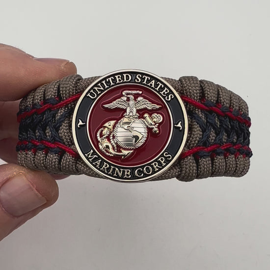 Thick, rigid and comfortable braided United States Marine Corps bracelet featuring a 24K gold and silver plated USMC officer Eagle Globe and Anchor medallion, a gold Cobra style tactical buckle and woven with tan 550 paracord and Imperial Red and Navy Blue micro cord.