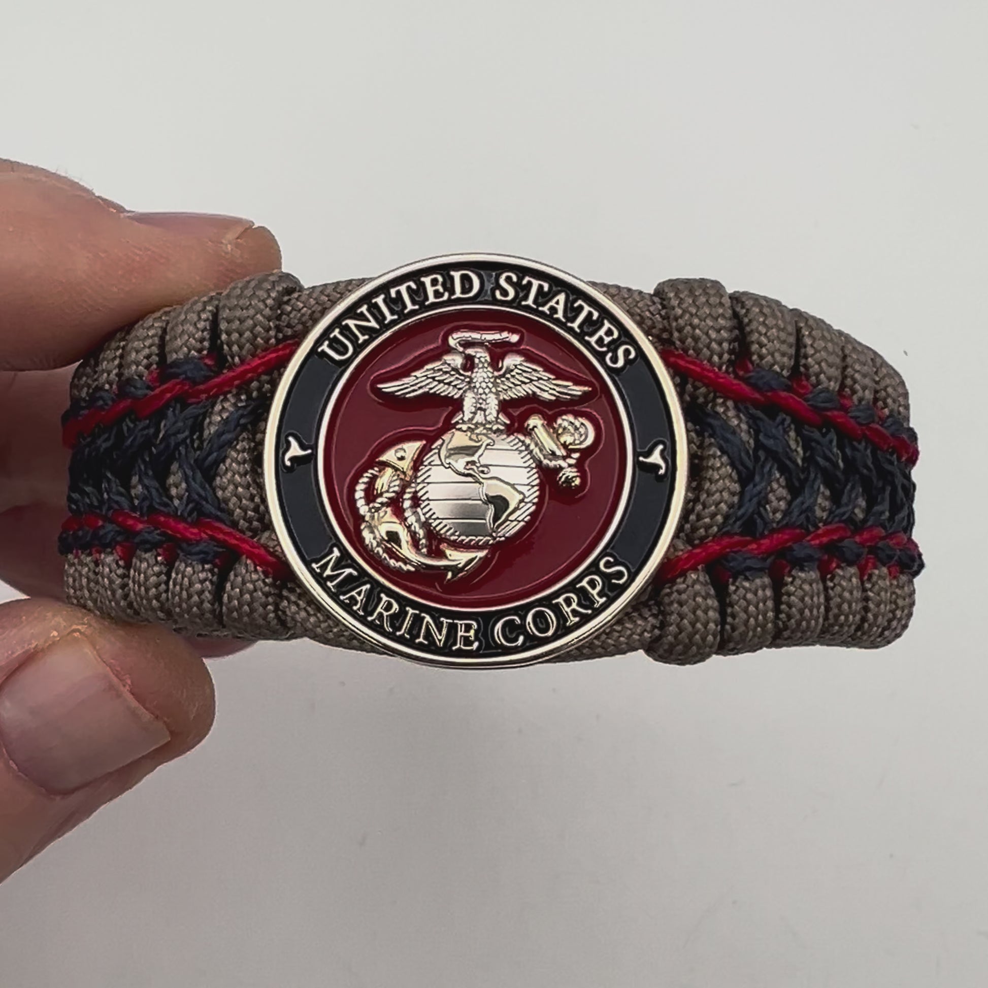 Thick, rigid and comfortable braided United States Marine Corps bracelet featuring a 24K gold and silver plated USMC officer Eagle Globe and Anchor medallion, a gold Cobra style tactical buckle and woven with tan 550 paracord and Imperial Red and Navy Blue micro cord.