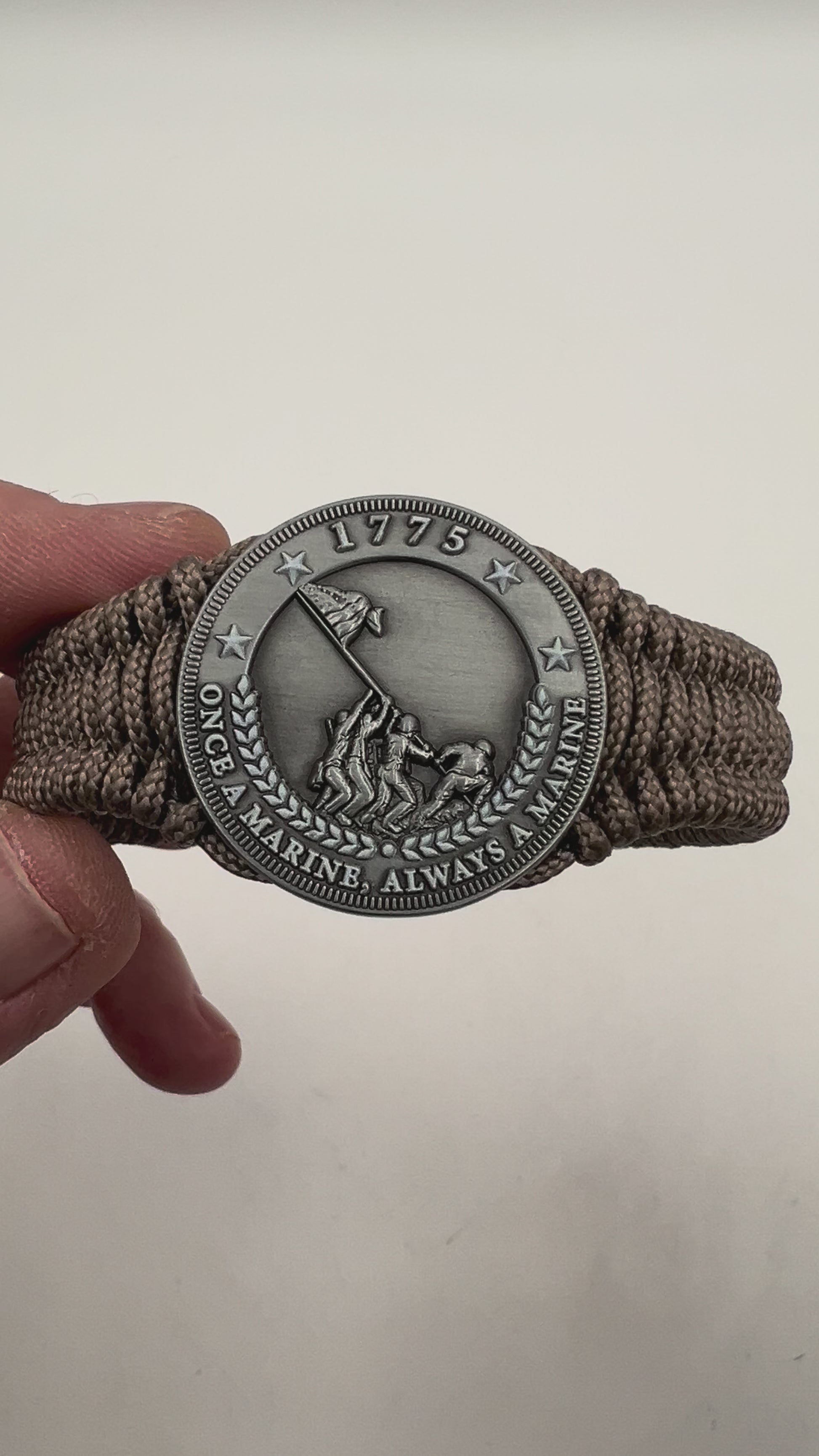 Thin, narrow, flexible and comfortable braided United States Marine Corps Iwo Jima bracelet featuring an antique silver plated Iwo Jima flag raising medallion, a silver Cobra style tactical buckle and woven with tan type-1 paracord.