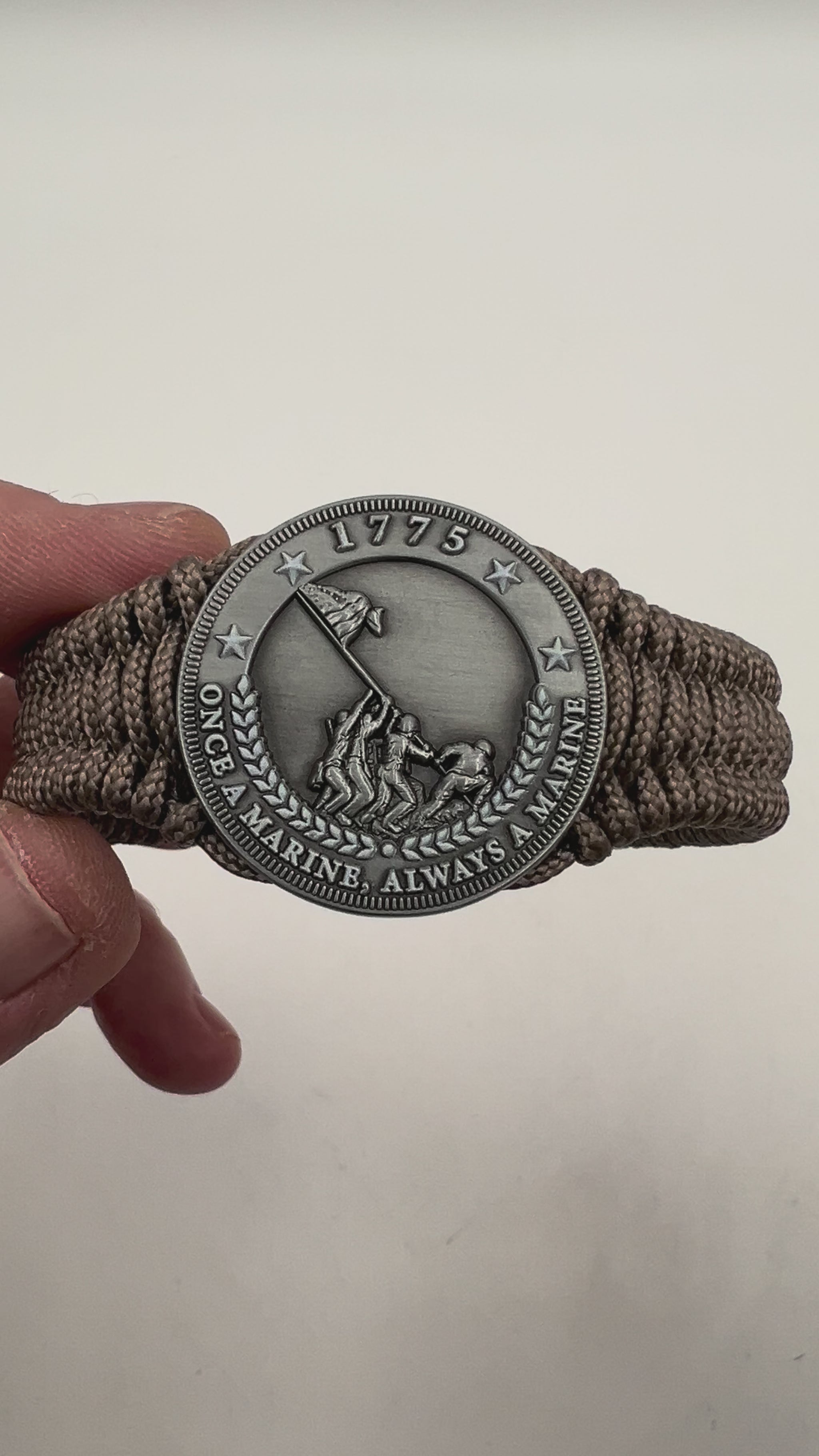 Thin, narrow, flexible and comfortable braided United States Marine Corps Iwo Jima bracelet featuring an antique silver plated Iwo Jima flag raising medallion, a silver Cobra style tactical buckle and woven with tan type-1 paracord.