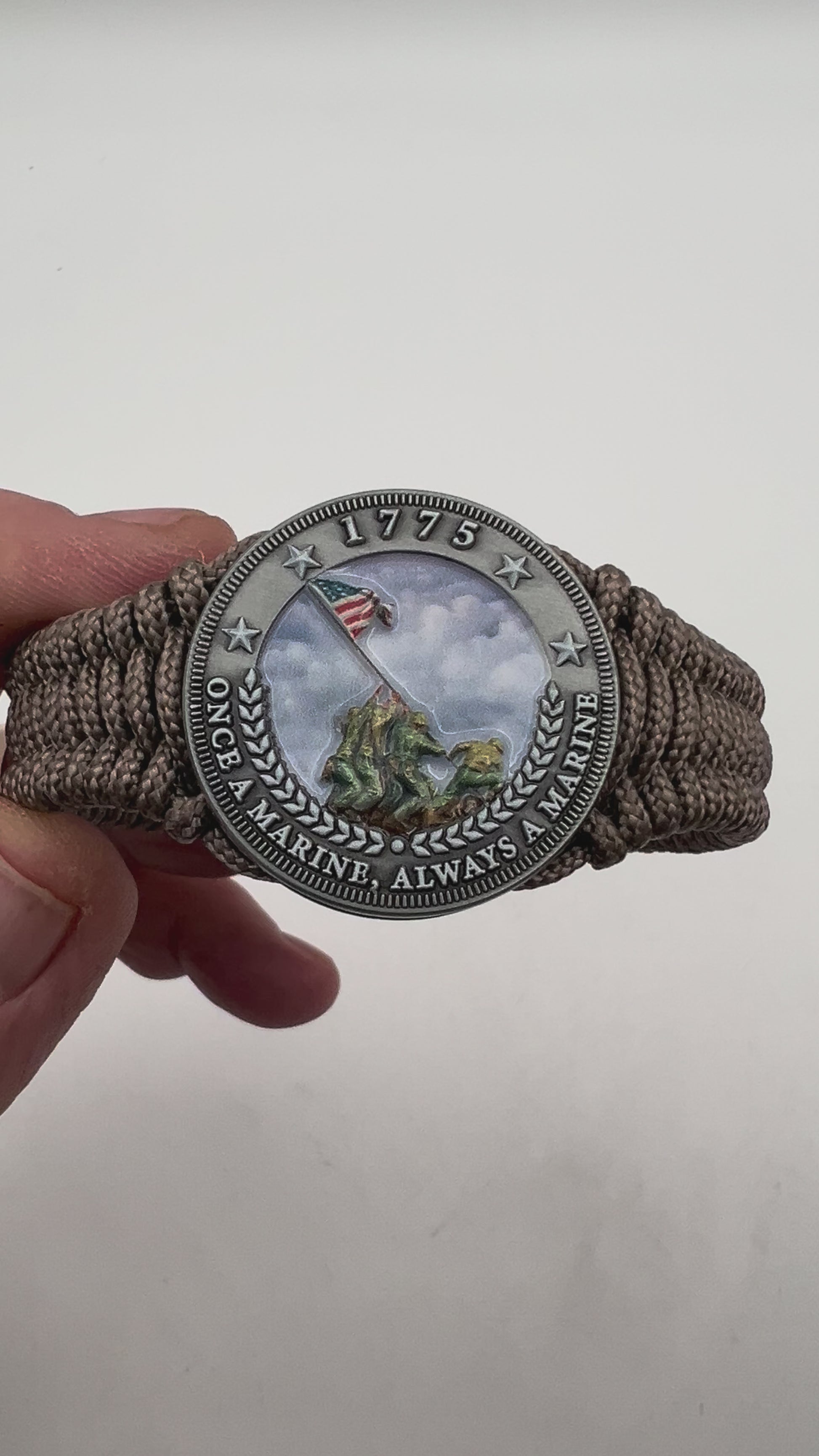 Thin, narrow, flexible and comfortable braided United States Marine Corps Iwo Jima bracelet featuring an antique silver plated UV painted Iwo Jima flag raising medallion, a silver Cobra style tactical buckle and woven with tan type-1 paracord.