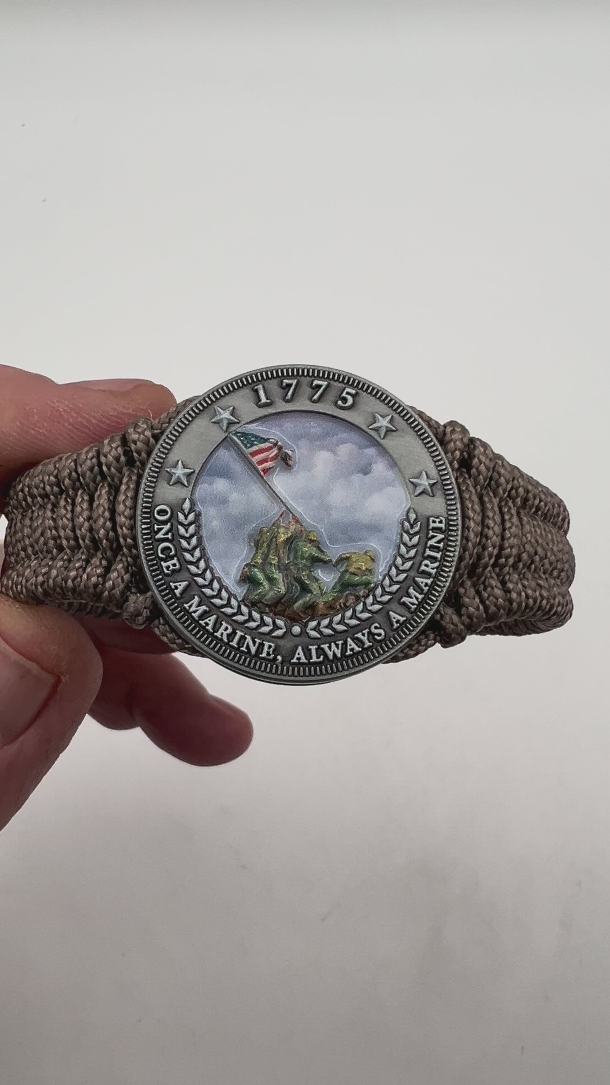 Thin, narrow, flexible and comfortable braided United States Marine Corps Iwo Jima bracelet featuring an antique silver plated UV painted Iwo Jima flag raising medallion, a silver Cobra style tactical buckle and woven with tan type-1 paracord.