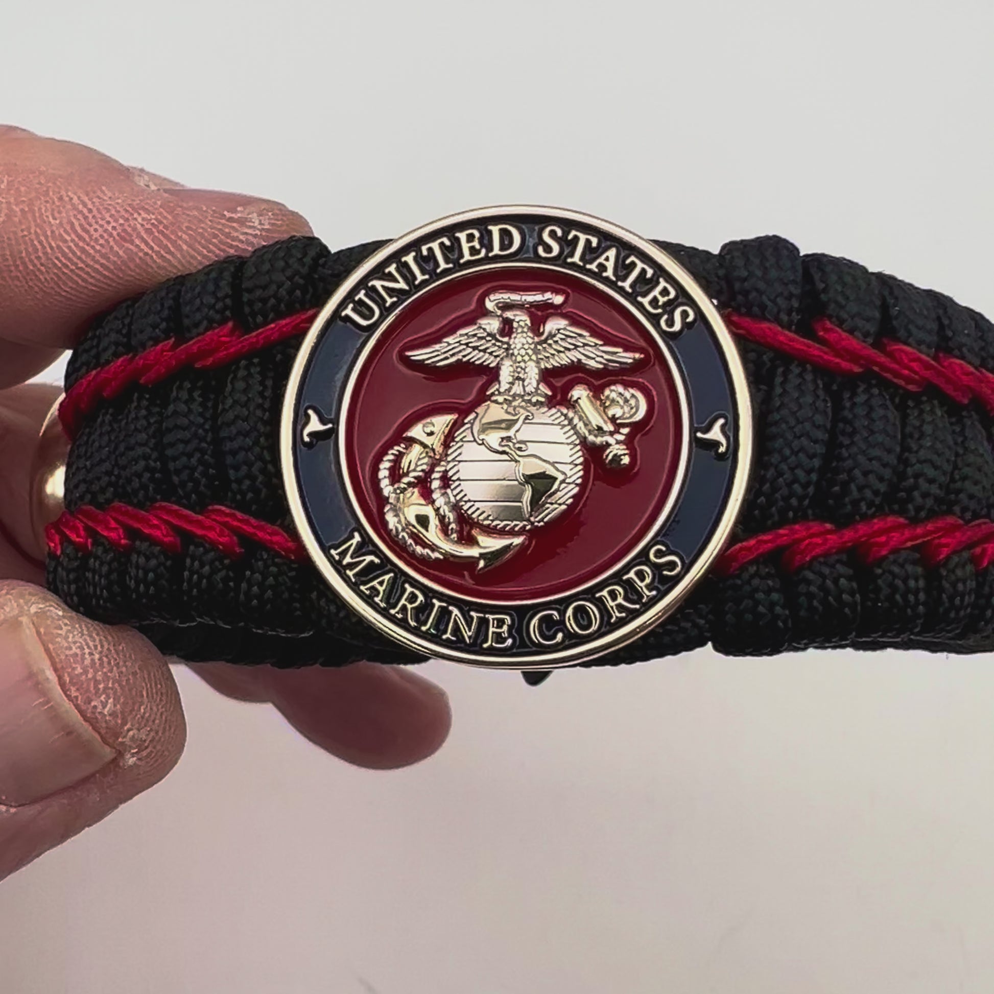 Thick and comfortable braided United States Marine Corps bracelet featuring a 24K gold and silver plated USMC officer Eagle Globe and Anchor medallion, a black Cobra style tactical buckle and woven with black 550 paracord and Imperial Red micro cord.