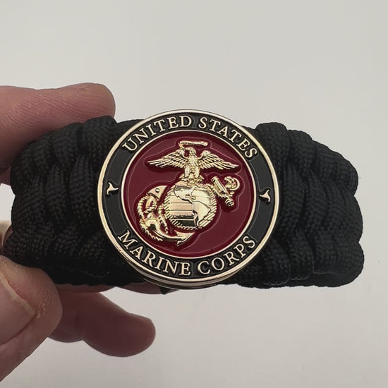 Thick, wide, rigid and comfortable braided United States Marine Corps bracelet featuring a 24K gold plated USMC Eagle Globe and Anchor medallion, a black Cobra style tactical buckle and woven with black 550 paracord.
