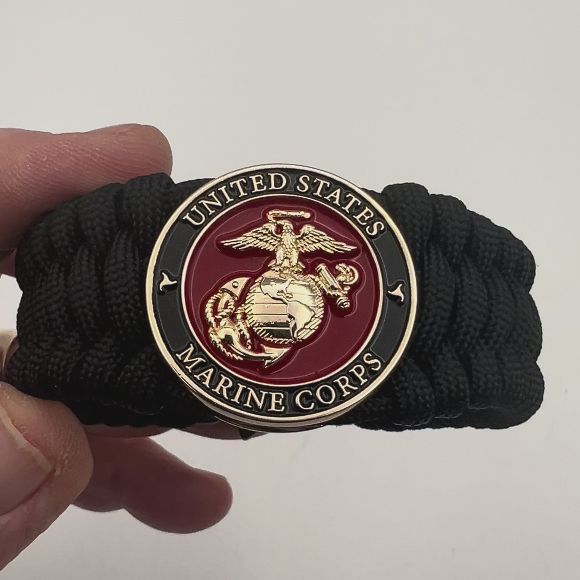 Thick, wide, rigid and comfortable braided United States Marine Corps bracelet featuring a 24K gold plated USMC Eagle Globe and Anchor medallion, a black Cobra style tactical buckle and woven with black 550 paracord.