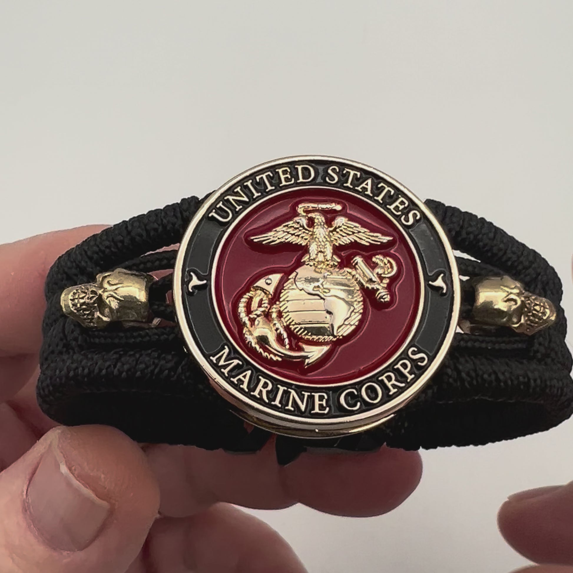 Thin, medium width, flexible and comfortable braided United States Marine Corps bracelet featuring a 24K gold plated USMC officer Eagle Globe and Anchor medallion, two gold plated skulls, a black Cobra style tactical buckle and woven with black Type-1 paracord.